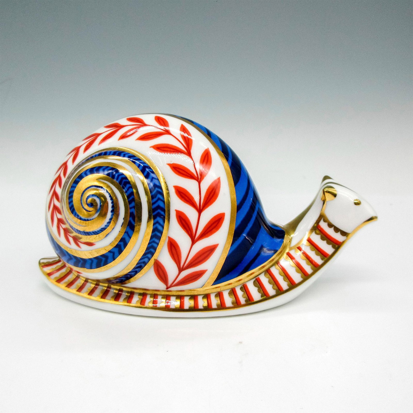 Royal Crown Derby Bone China Paperweight, Snail: Beautifully detailed figural colored in dark blue, rust and gilding throughout. Royal Crown Derby impressed mark on stopper and backstamp. XLIX. Issued: 20th century Dimensions: 5"L x 2.5"W x 3"H Manu