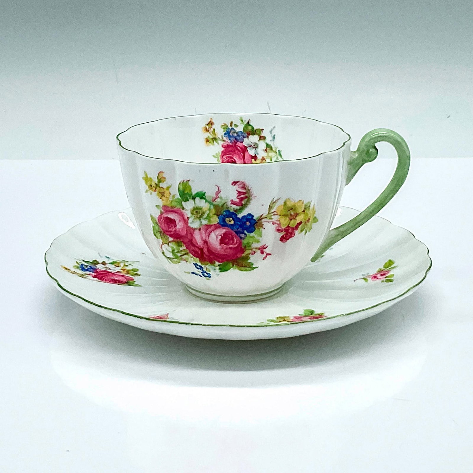 Shelley Fine Bone China Floral Tea Cup and Saucer: A floral ludlow shaped cup and saucer with green trims. Shelley backstamp and 13240 marked on the underside. Cup: 4.25"L x 3.25"W x 2.25"H. Saucer: 5.75"W x 0.75"H. Issued: 20th ce
