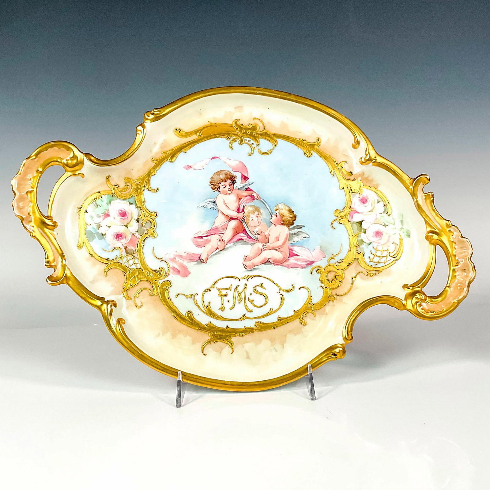 Tressemann & Vogt Limoges Porcelain F.M.S. Centerpiece: An elegant gilt tray centerpiece featuring two cherubs and roses. Monogram F.M.S. painted in gold. Tressemann & Vogt Limoges France backstamp. F.M.S. From A.T.C. March 25 1908 handwritten on the under