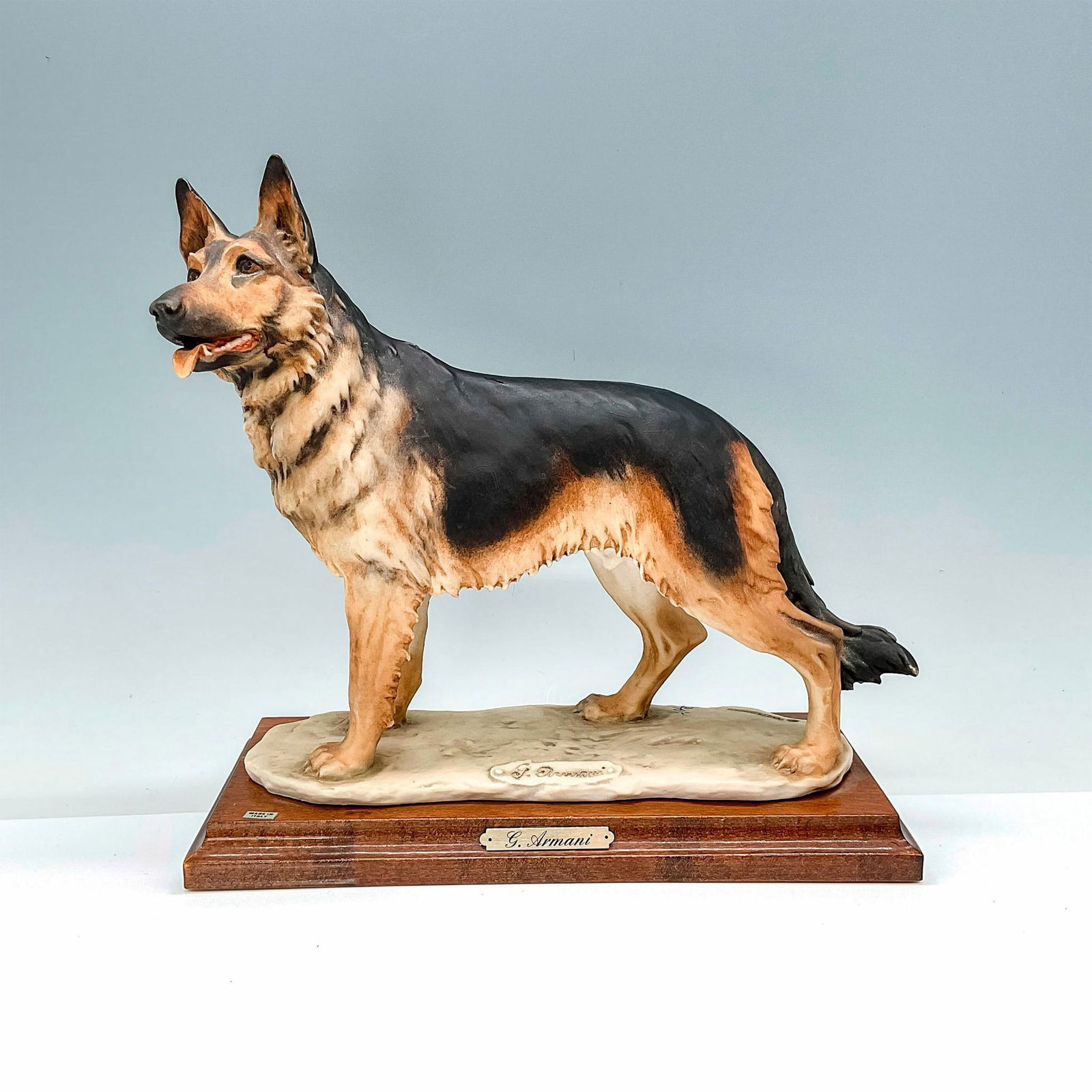 Florence Giuseppe Armani Figurine, German Shepherd: Dog figurine depicting a stoic German Shepherd. This figurine is attached to a wooden base. Florence carved into the base. G. Armani medallion attached to the base. Capodimonte backstamp to base. Issu