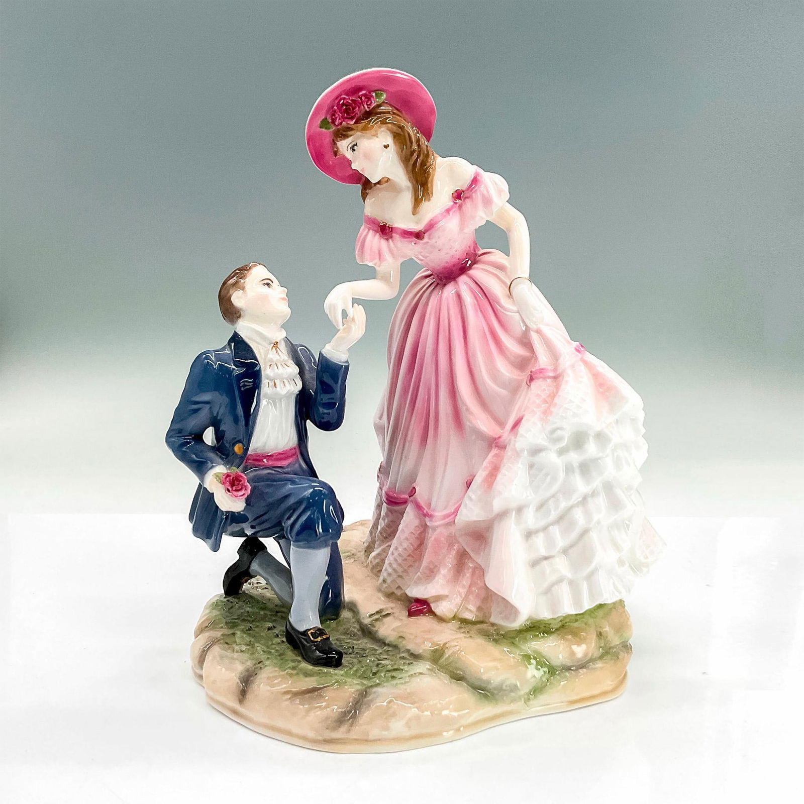 Royal Worcester Figurine, With Love, Age of Romance: Bone china figure of young man down on one knee gazing up at his beloved with a rose in his right hand. The man wears a dark cornflower blue suit. The lady wears a pink dress and hat. Royal Worcester