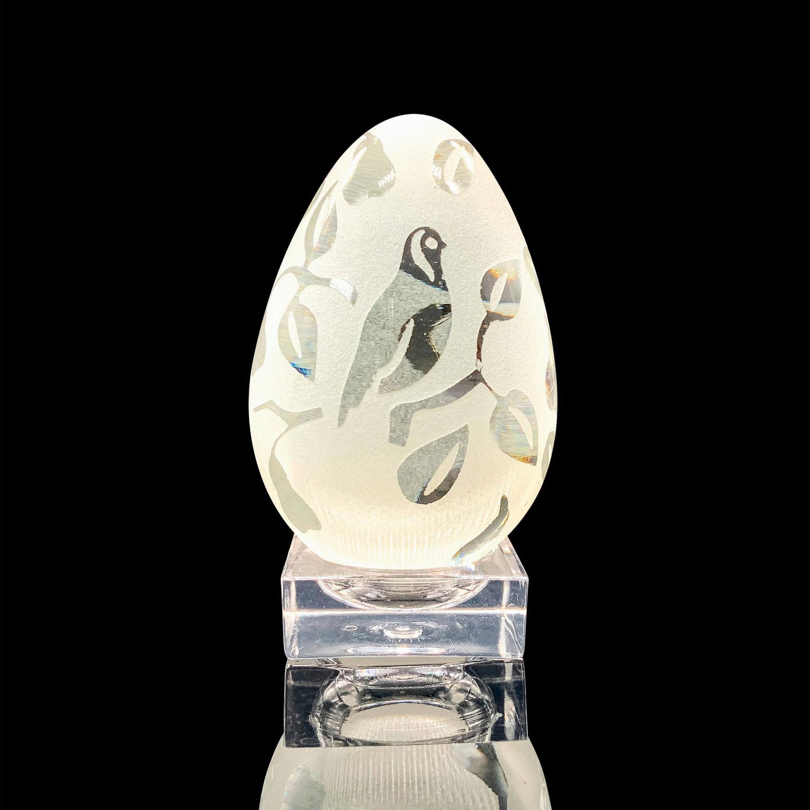 Frosted Crystal Egg Paperweight and Base: A frosted crystal egg paperweight that is designed with leaves, fruits, and a bird along with its clear base. Dimensions of the egg: 3"H x 1.75" dia. Dimensions of the base: 1.5"L x 1.5"W x 0.5"H. Dim
