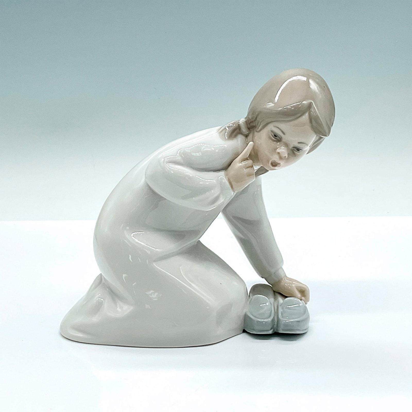 Little Girl with Slippers 1004523 - Lladro Porcelain Figurine: Glazed figure of a little girl over a pair of slippers. Lladro backstamp. Artist: Vincente Martinez Issued: c. 1969-1993 Dimensions: 5.25"L x 2.5"W x 5.25"H Manufacturer: Lladro Country of Origin: