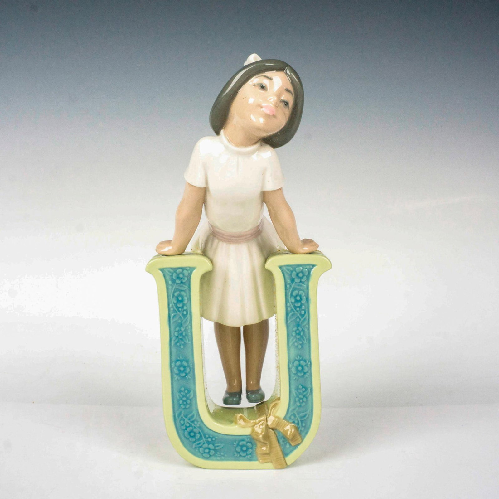 Schoolgirl U 1005149 - Lladro Porcelain Figurine: Glossy finish; Lladro backstamp. Includes original box. Box measures: 10.75"L x 5.5"W x 5"H. Artist: Jose Puche Issued: 1982 - 1985 Dimensions: 7.75"H Manufacturer: Lladro Country of Origin: Sp