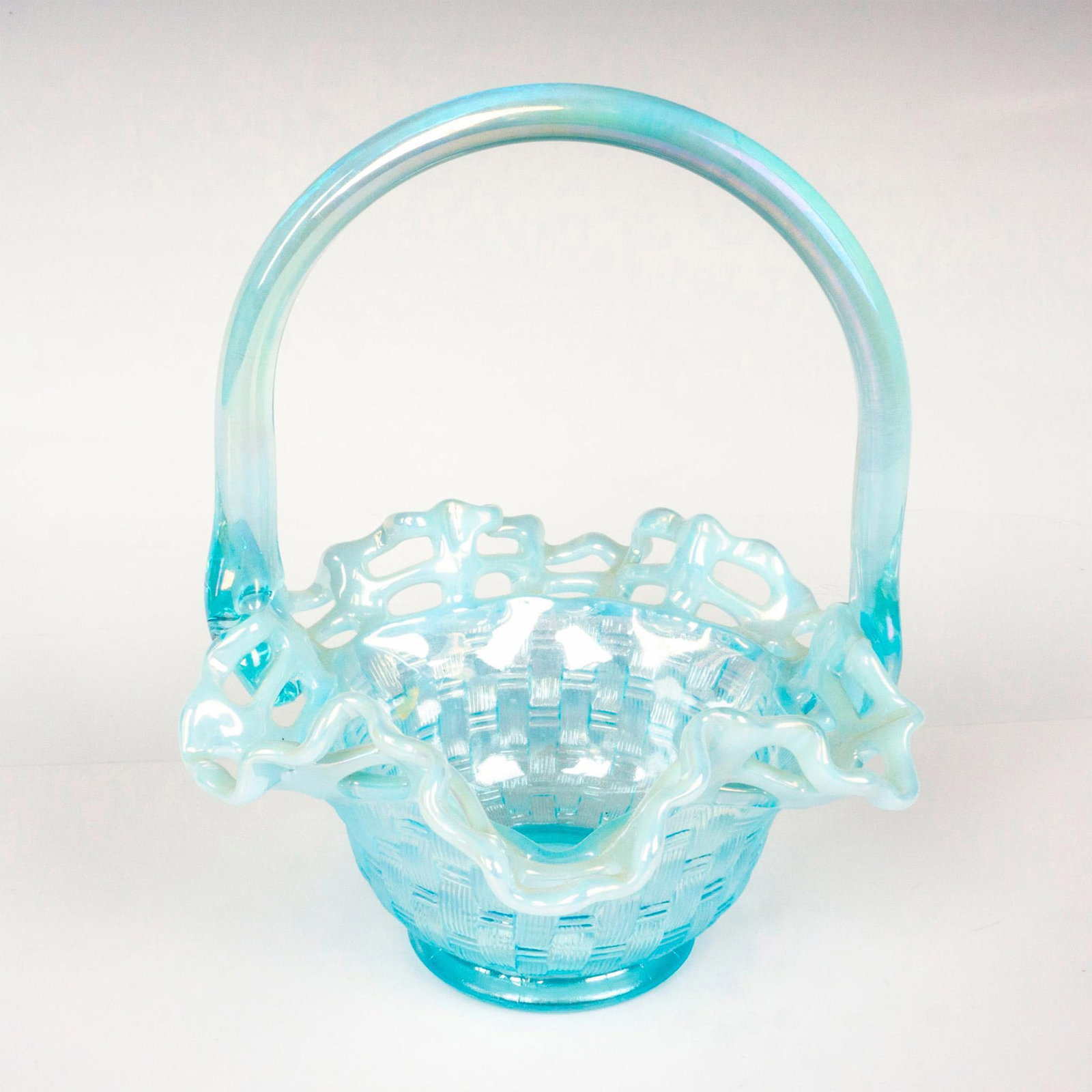 Fenton Glass Weave Basket: An opalescent bowl with textured pattern and scallop rim; applied handle. Fenton impressed backstamp. Dimensions: 5.5"L x 6"W x 7.5"H Manufacturer: Fenton Country of Origin: United States Condition</