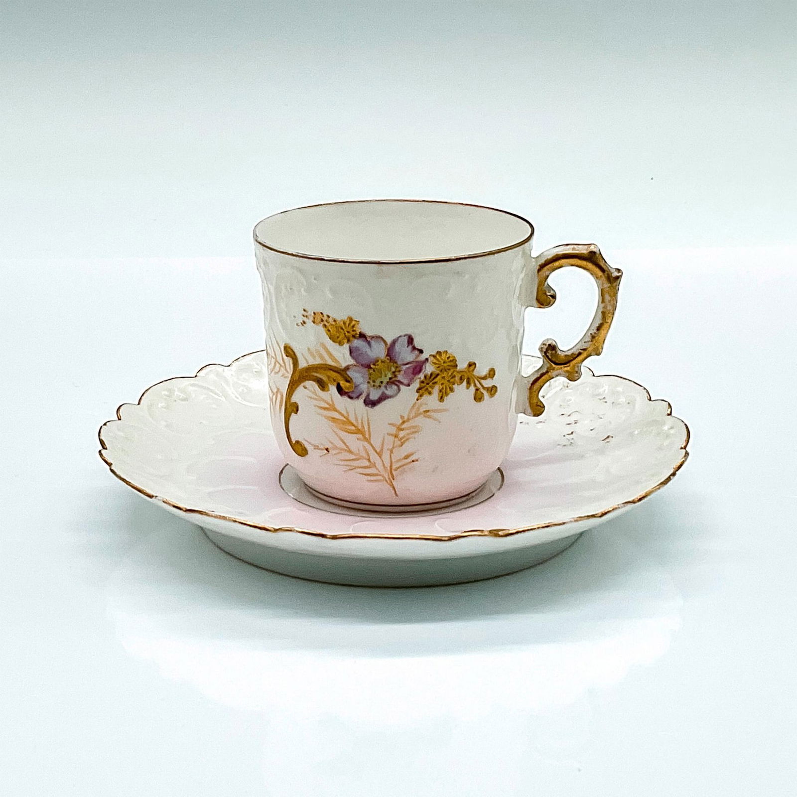Elite Limoges Porcelain Espresso Cup and Saucer: A beautiful pink and white demitasse set with hand-painted purple and gold flowers, and embossed reliefs. Elite Limoges backstamps. Cup: 3"L x 2.25"W x 2"H. Saucer: 0.75"H x 4.75"dia. Issued: 1896-190