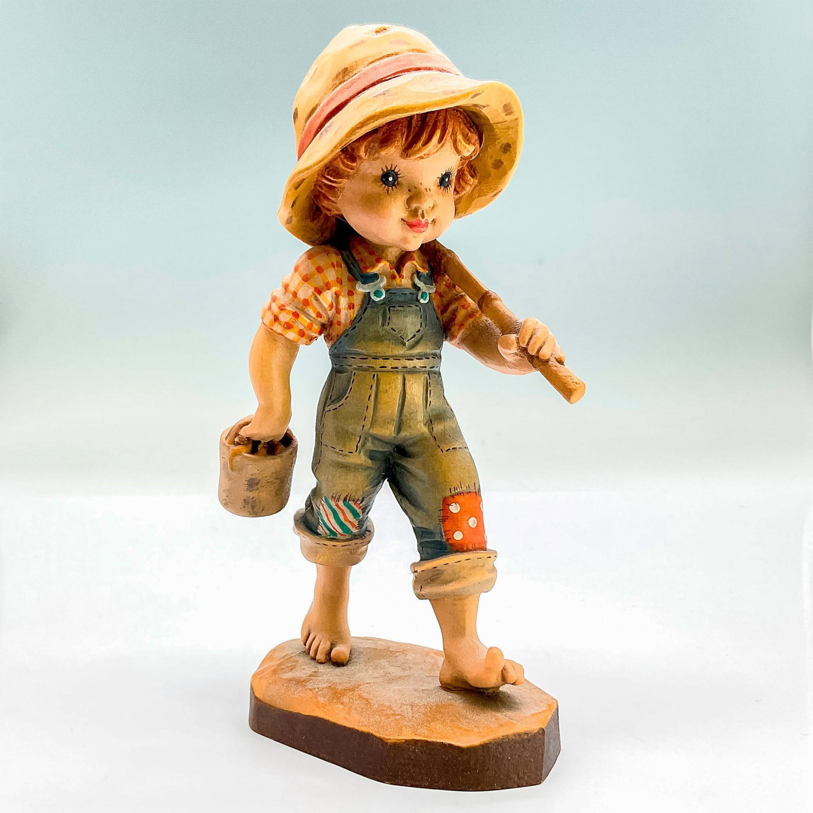 Anri Italy Wood Carved Figurine, Fisherboy: Painted figure of a plucky young boy in a hat holding a bucket in one hand and a fishing rod in the other. In hues of earthy orange, blue, tan and brown. Anri metal logo emblem affixed to base. Design