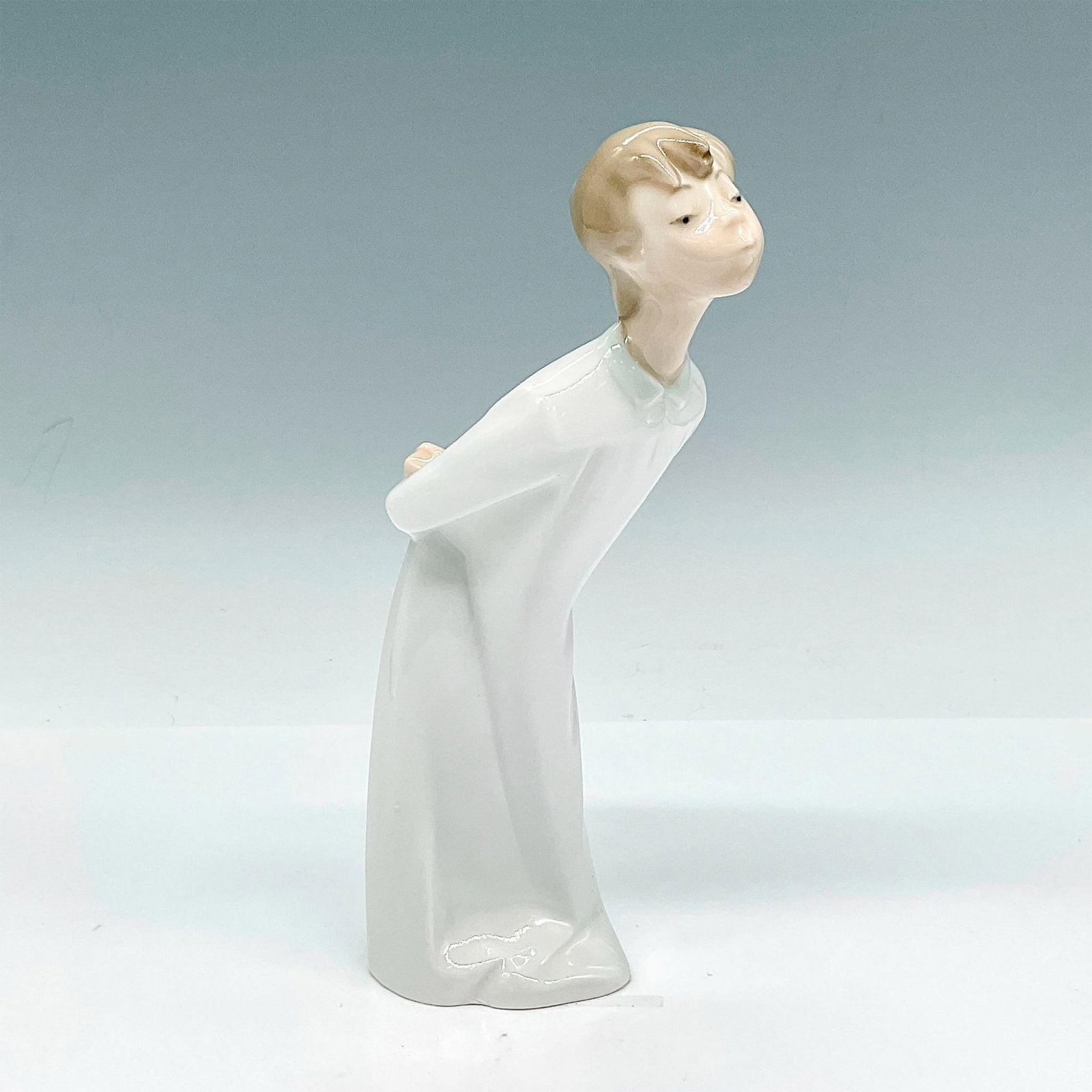 Boy Kissing 1004869 - Lladro Porcelain Figurine: Glossy figure of boy in a white robe leaning over for a kiss. Lladro backstamp. Artist: Fulgencio Garcia Issued: 20th Century Dimensions: 4.5"L x 2.5"W x 7.75"H Manufacturer: Lladro Country of Origin