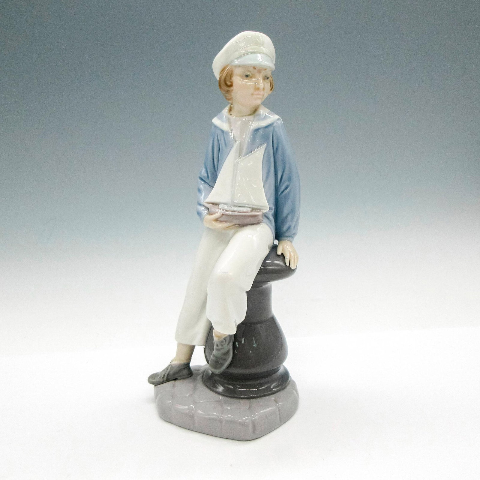 Boy With Yacht 1004810 - Lladro Porcelain Figurine: Glossy finish; Lladro backstamp. Artist: Salvador Furio Issued: 1972 - 1998 Dimensions: 9"H Manufacturer: Lladro Country of Origin: Spain