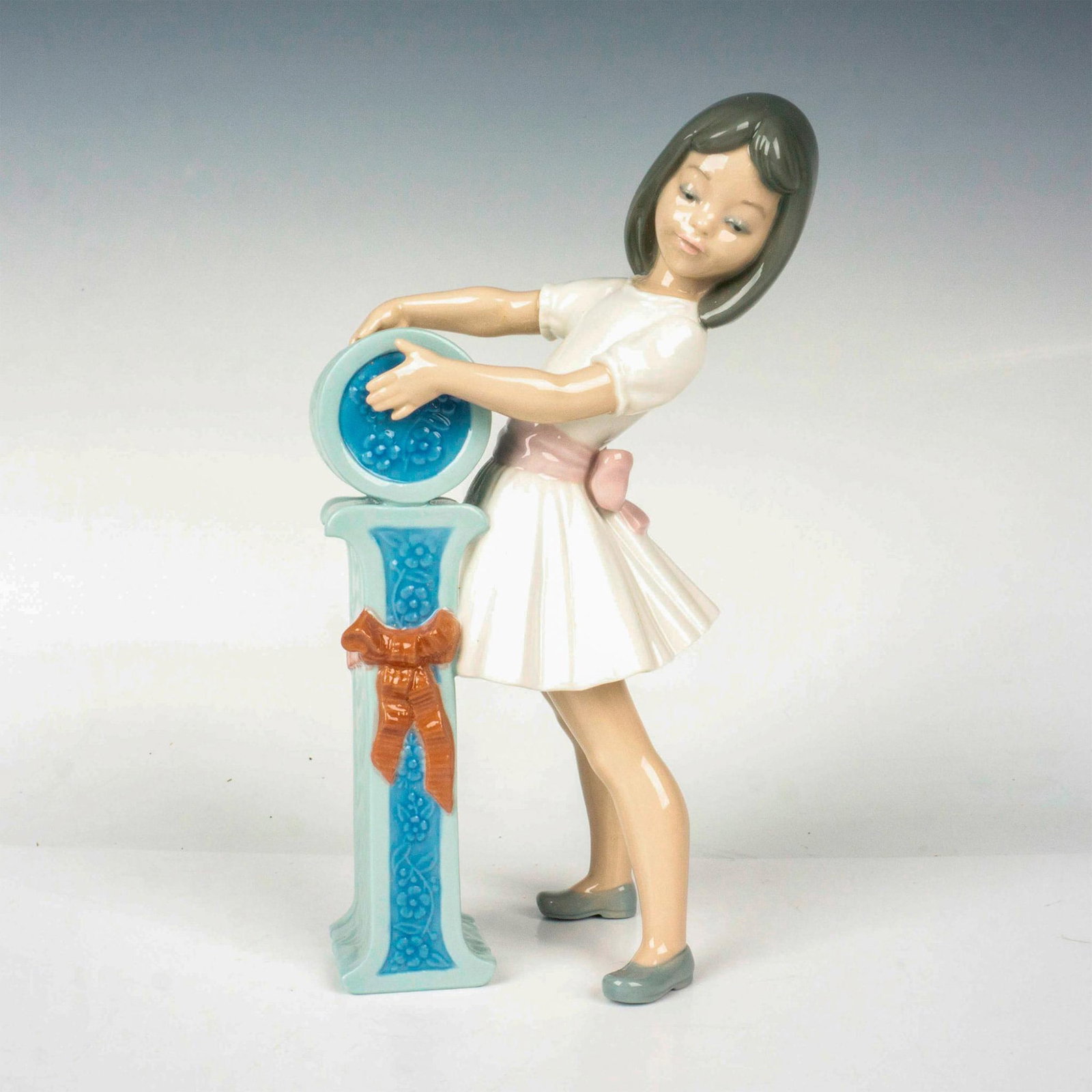 Schoolgirl I 1005147 - Lladro Porcelain Figurine: Glossy finish; Lladro backstamp. Includes original box. Box measures: 10.75"L x 5.5"W x 5"H. Artist: Jose Puche Issued: 1982 - 1985 Dimensions: 7.75"H Manufacturer: Lladro Country of Origin: Spain