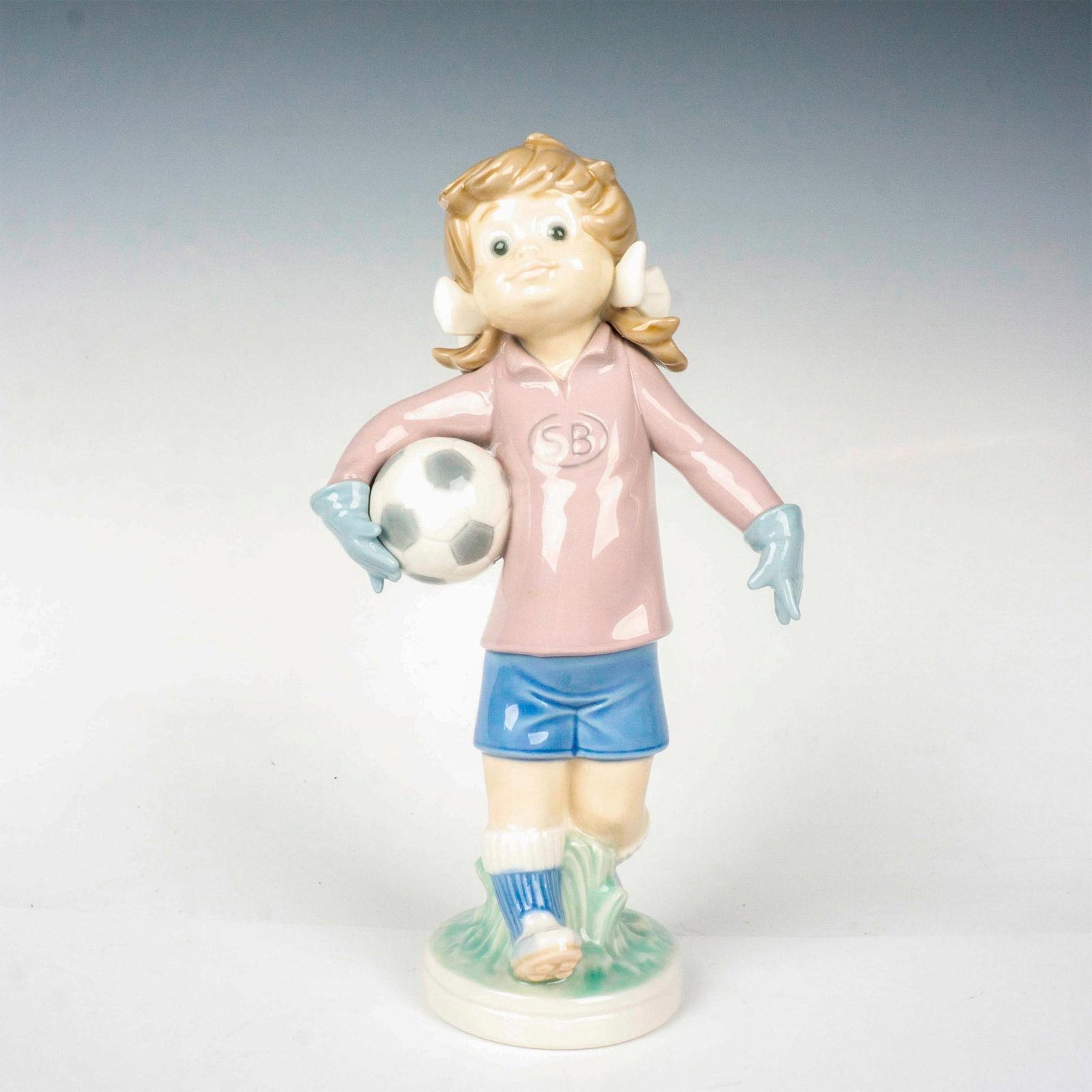 Sports Lilly Football 1005134 - Lladro Porcelain Figurine: Glossy finish; Lladro backstamp. Includes original box. Box measures: 12.25"L x 7.25"W x 5.75"H. Artist: Jose Roig Issued: 1982 - 1983 Dimensions: 9"H Manufacturer: Lladro Country of Origin: Spain