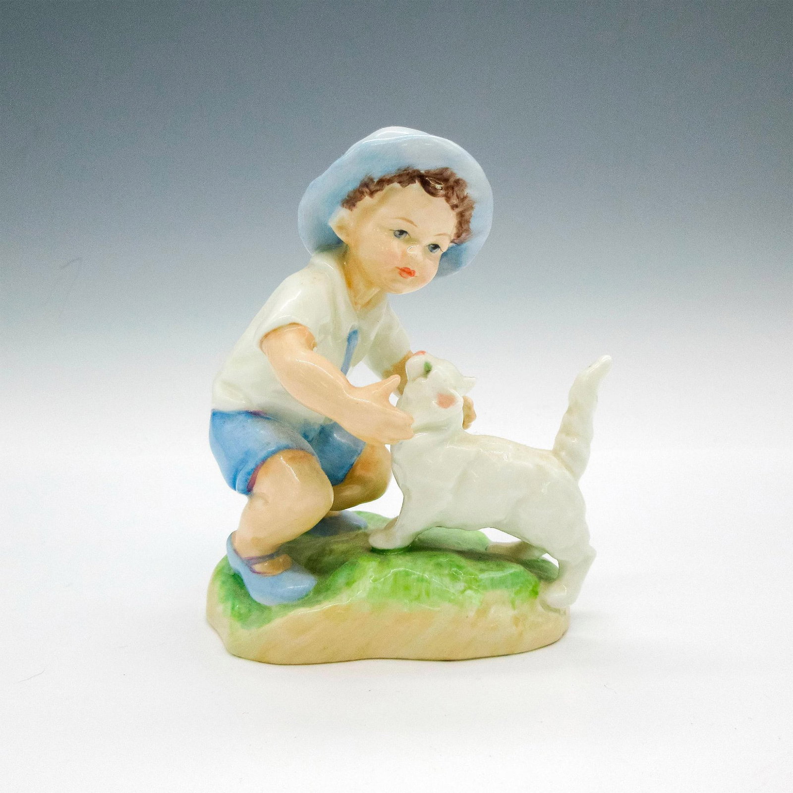 Royal Worcester Bone China Figurine, September: Part of Month of the Year series. Child dressed in light blue hat, shoes and shorts playing with cat. Royal Worcester backstamp. 3457. Artist: F.G. Doughty Issued: 20th century Dimensions: 3.75"L x 3"