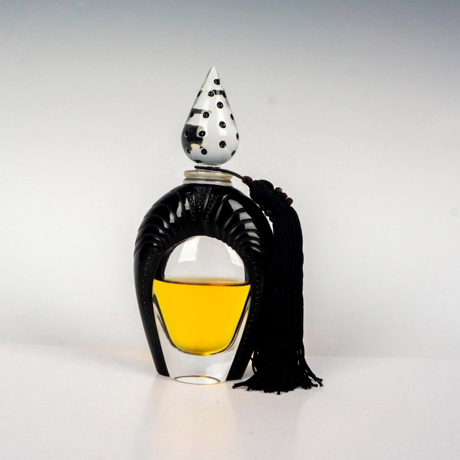 Lalique France Perfume Bottle, Sheherazade: An attractive, limited edition featuring a black glass border body. Includes clear glass topper with black polka dots and a tassel. Lalique factory label. Lalique France etched backstamp. Issued: 2008