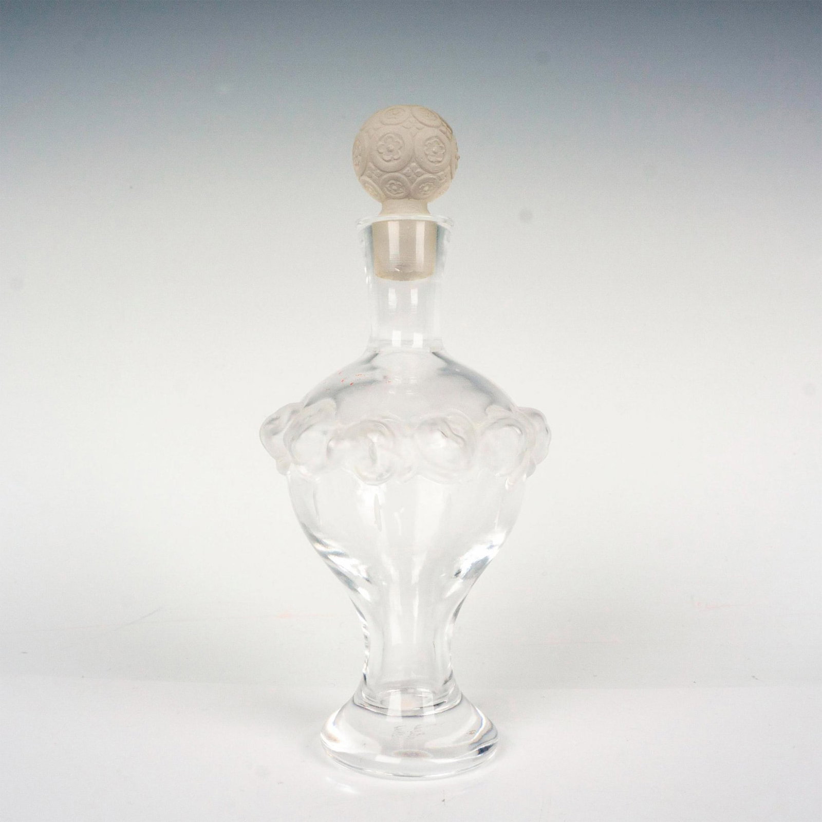 Lalique Crystal Perfume Bottle, Martine: A clear and frosted vessel embossed with roses around body. Includes a frosted stopper decorated with flowers. Lalique France etched backstamp. Dimensions: 2.5"W x 6.5"H Country of Origin: France Manu