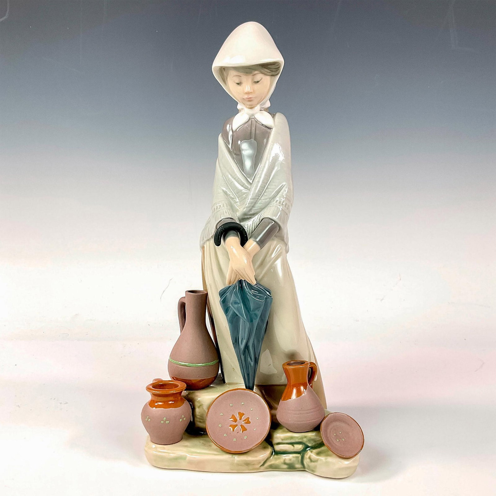 Ceramic Seller Woman 1005081 - Lladro Porcelain Figurine: Glossy finish; Lladro backstamp. Artist: Juan Huerta Issued: 1980 - 1985 Dimensions: 11.75"H Manufacturer: Lladro Country of Origin: Spain
