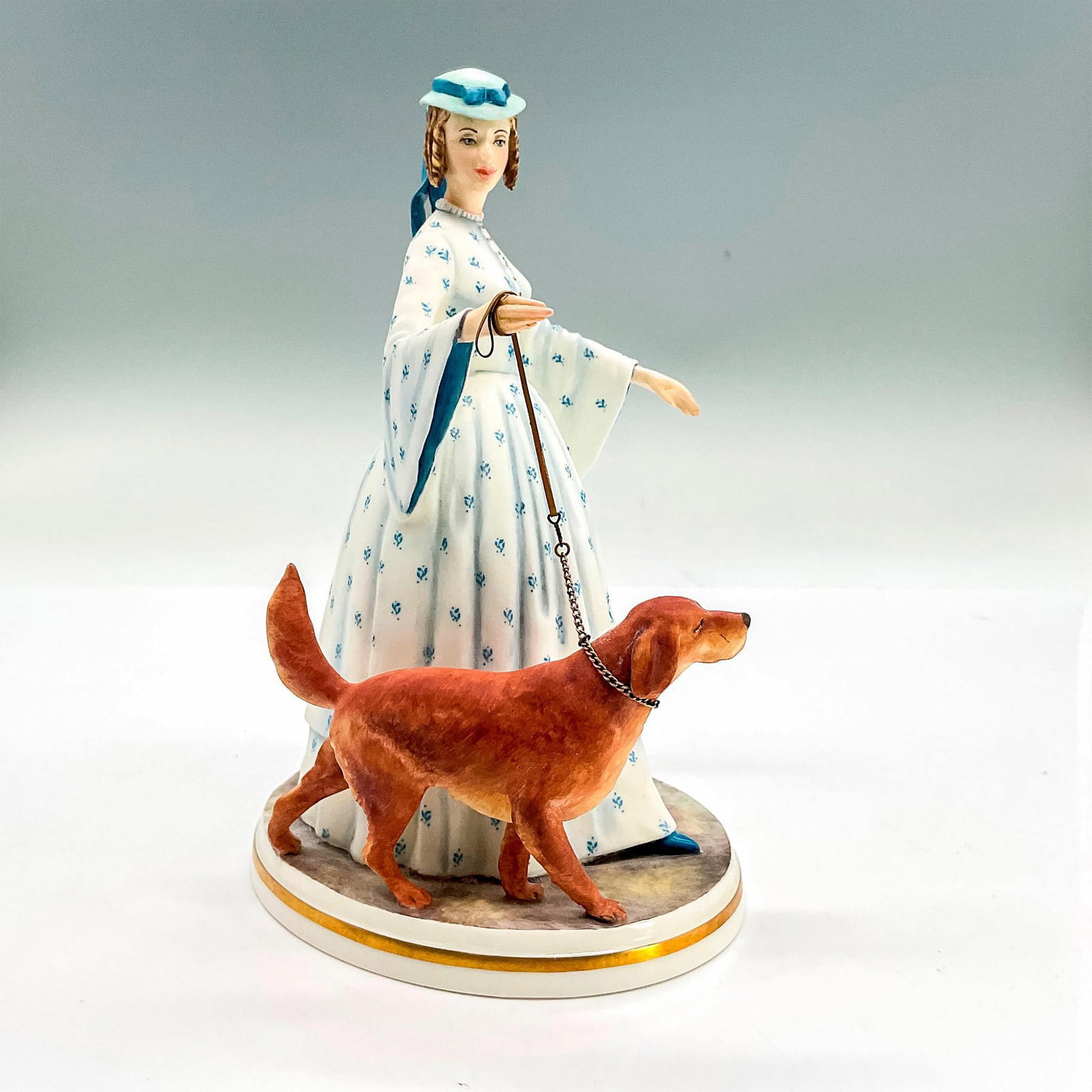 Royal Worcester Figurine, Felicity: Matte bone china figure of a lady in a light blue dress and hat walking her brown dog. Royal Worcester backstamp. Part of the Victorian Series, No. 243. Issued: 1970 Dimensions: 5"L x 4"W x 7"H Manufa