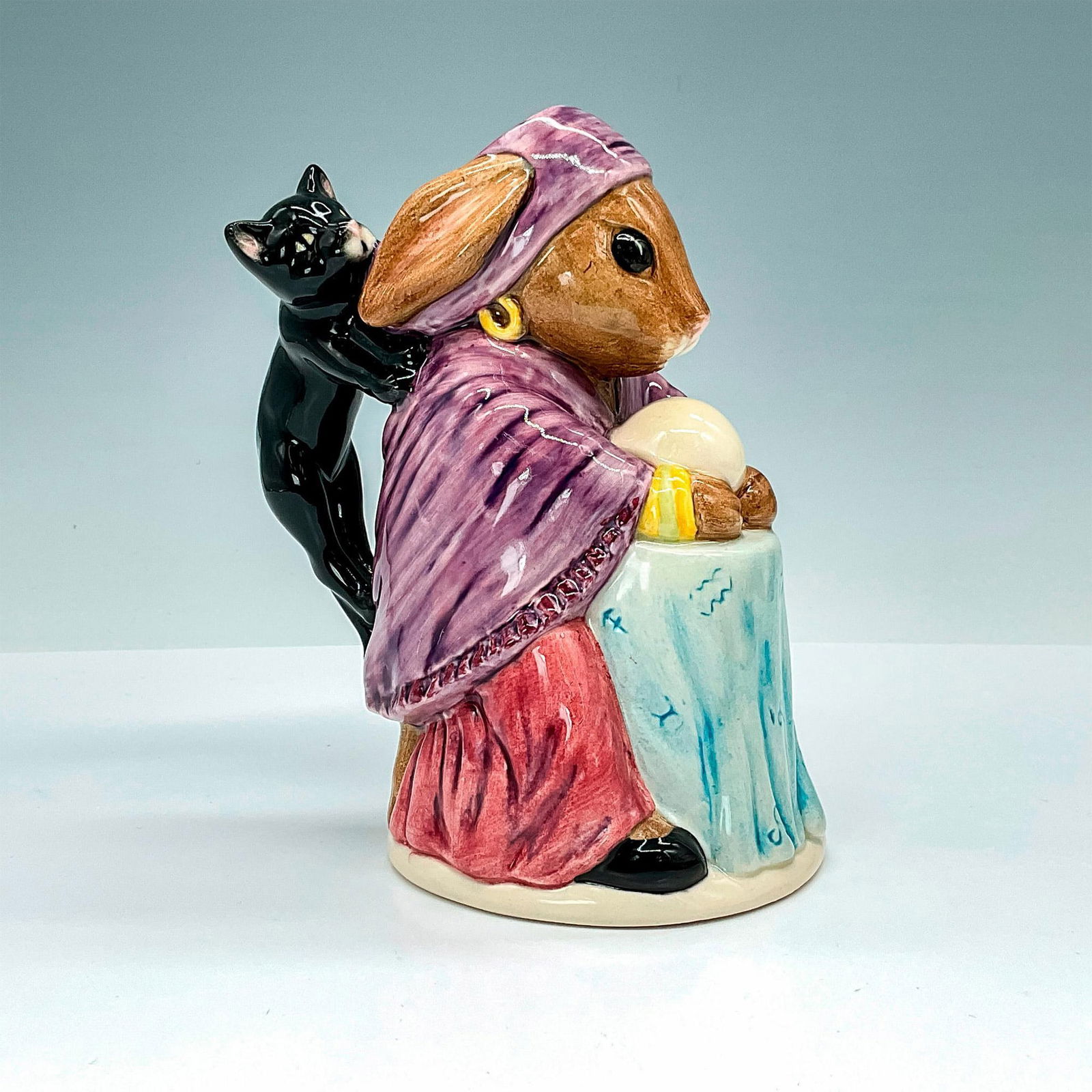 Royal Doulton Toby Jug, Fortune Teller D7157: This magical toby jug features a bunny fortune teller with a crystal ball and a black cat as the handle. Issued in 1999, it showcases a bunny holding a crystal ball in colors of black, blue, brown, ma