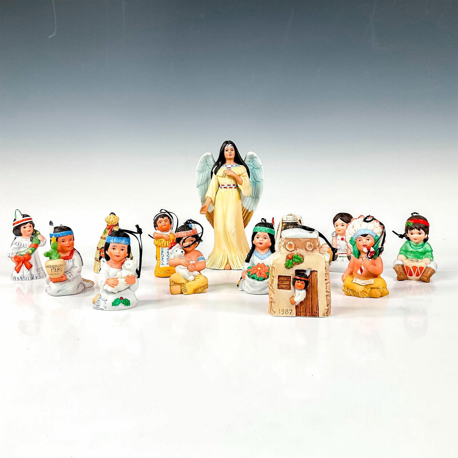 13pc Ceramic Annual Edition Holiday Christmas Ornament Set: Tree adornments depicting figural Native American children and an angel with festive Christmas holiday symbols. Vague Shadows backstamp. Largest piece includes: 4.25"L x 2.5"W x 7.5"H. Issued: c. 1985