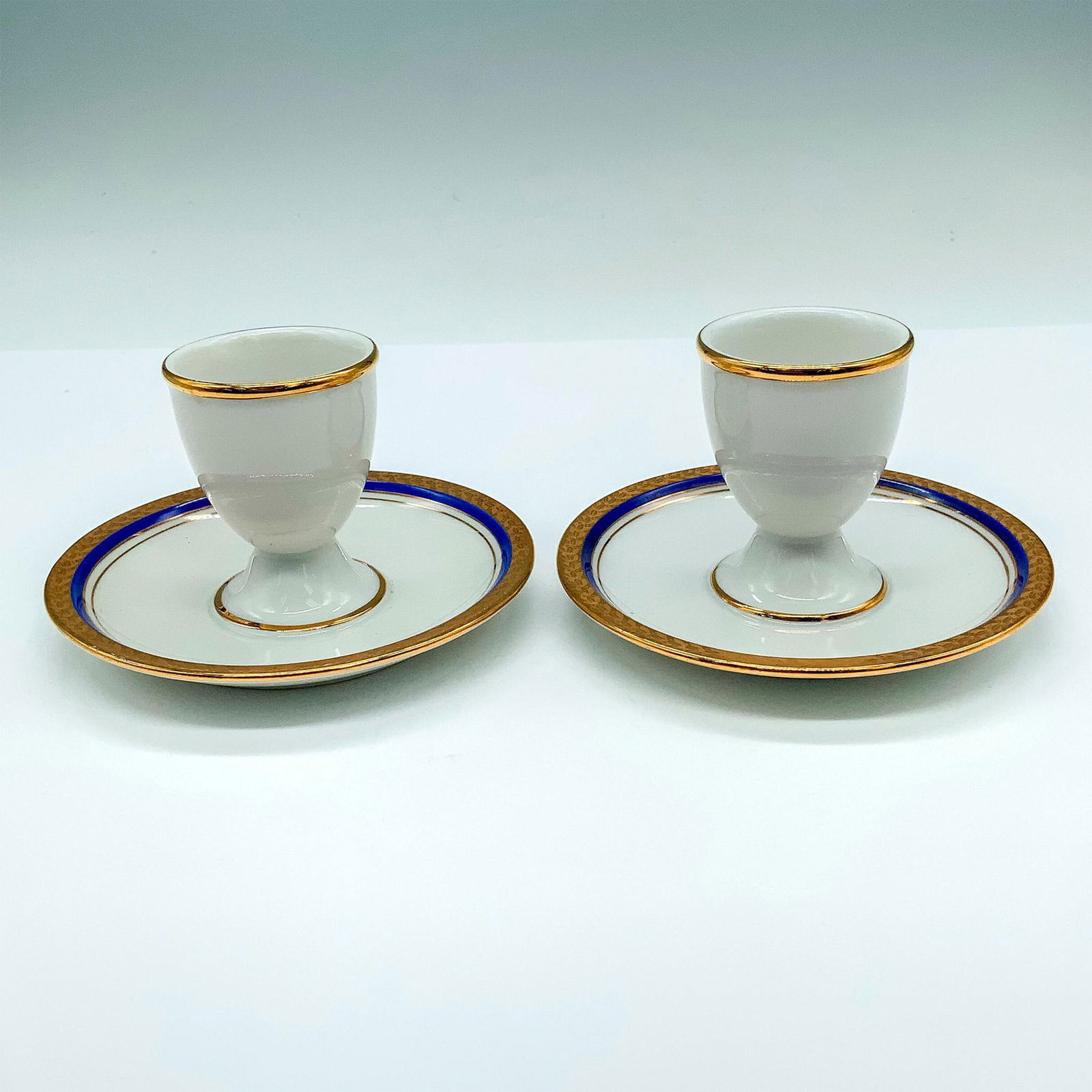 Pair of Rosenthal Egg Cups with Attached Underplates: White porcelain egg holders with blue and gold trim. Dimensions: 4.75"dia. x 2.75"H Manufacturer: Rosenthal Country of Origin: Germany