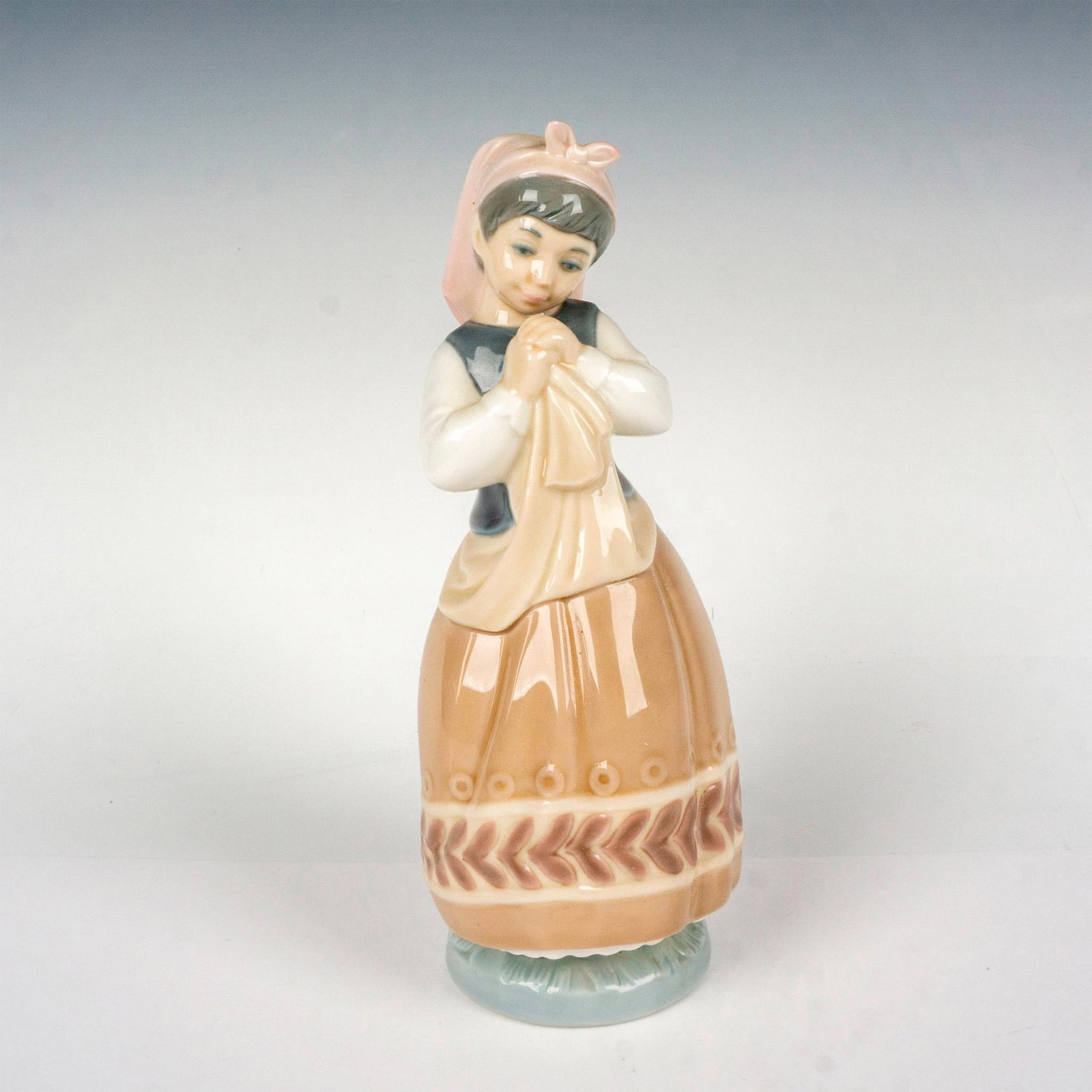 Blushful Girl 1005026 - Lladro Porcelain Figurine: Glossy finish; Lladro backstamp. Artist: Julio Fernandez Issued: 1980 - 1985 Dimensions: 8.75"H x 4"W Manufacturer: Lladro Country of Origin: Spain