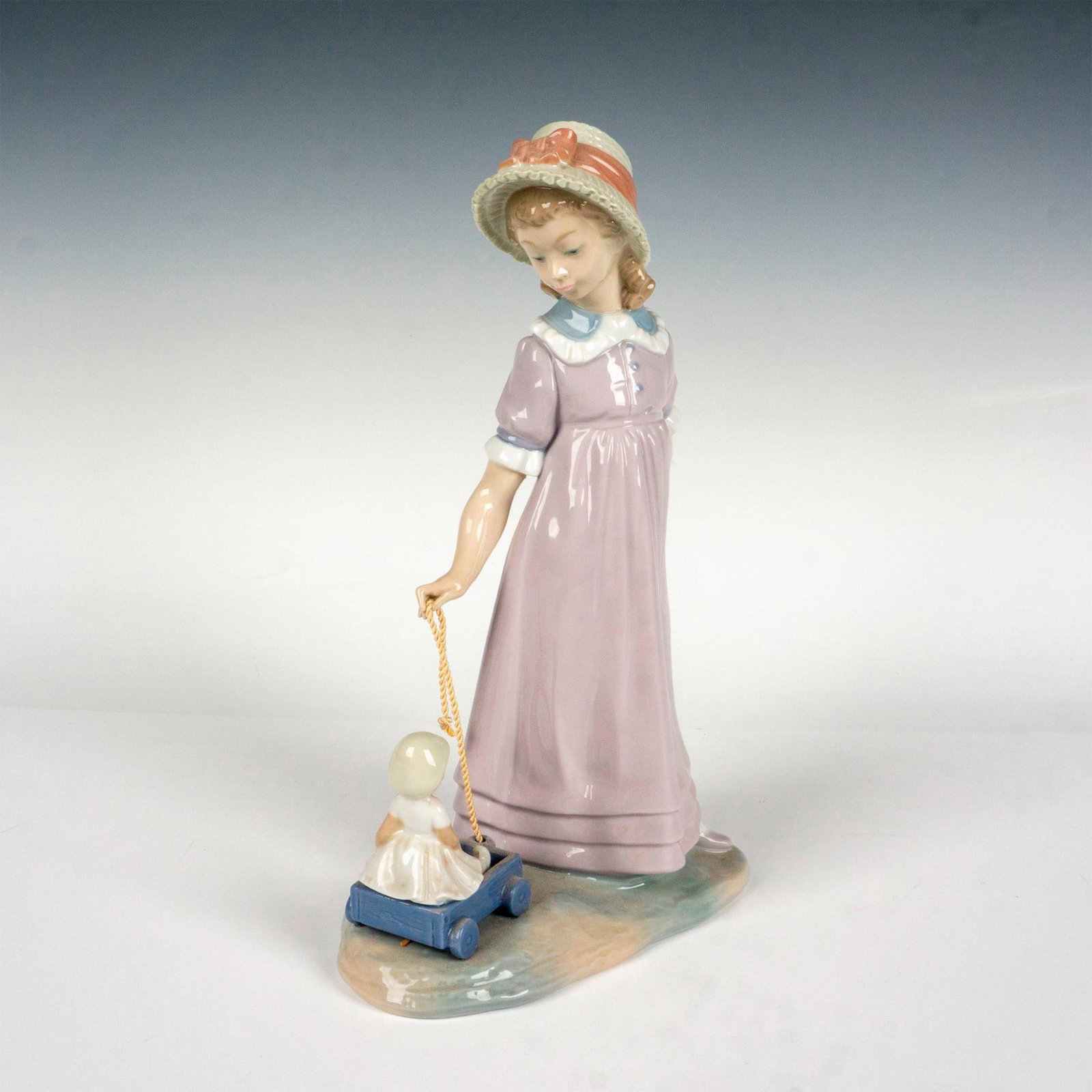 Girl With Toy Wagon 1005044 - Lladro Porcelain Figurine: Glossy finish; Lladro backstamp. Artist: Vicente Martinez Issued: 1980 - 1997 Dimensions: 11"H x 6.75"W Manufacturer: Lladro Country of Origin: Spain
