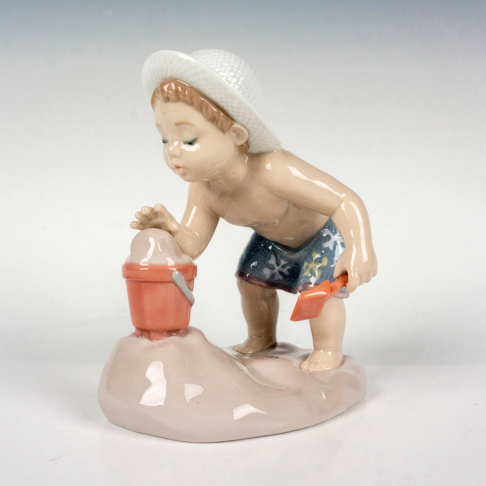 Playing In The Sand 1008440 - Lladro Porcelain Figurine: Glossy finish; Lladro backstamp. Includes original box. Box measures 7.25"L x 8"W x 4.75"H. Artist: Jose Santaeulalia Issued: 2009 - 2017 Dimensions: 4.75"H x 4.75"W Manufacturer: Lladro Country of Or