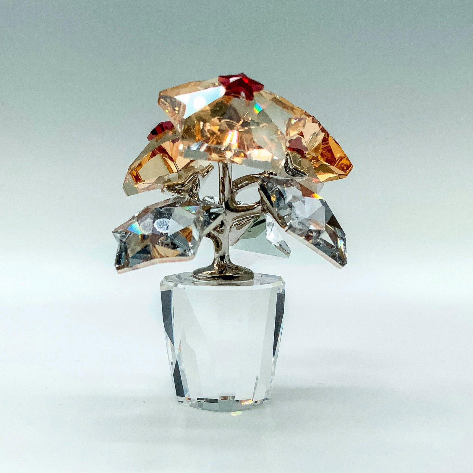 Swarovski Crystal Figurine, Star Blossoms 1006036: A figure depicting a pot of flowers that have the flowers in the shape of stars with some being clear and the others being amber colored. Swarovski backstamp. This item has its original box. Dimension