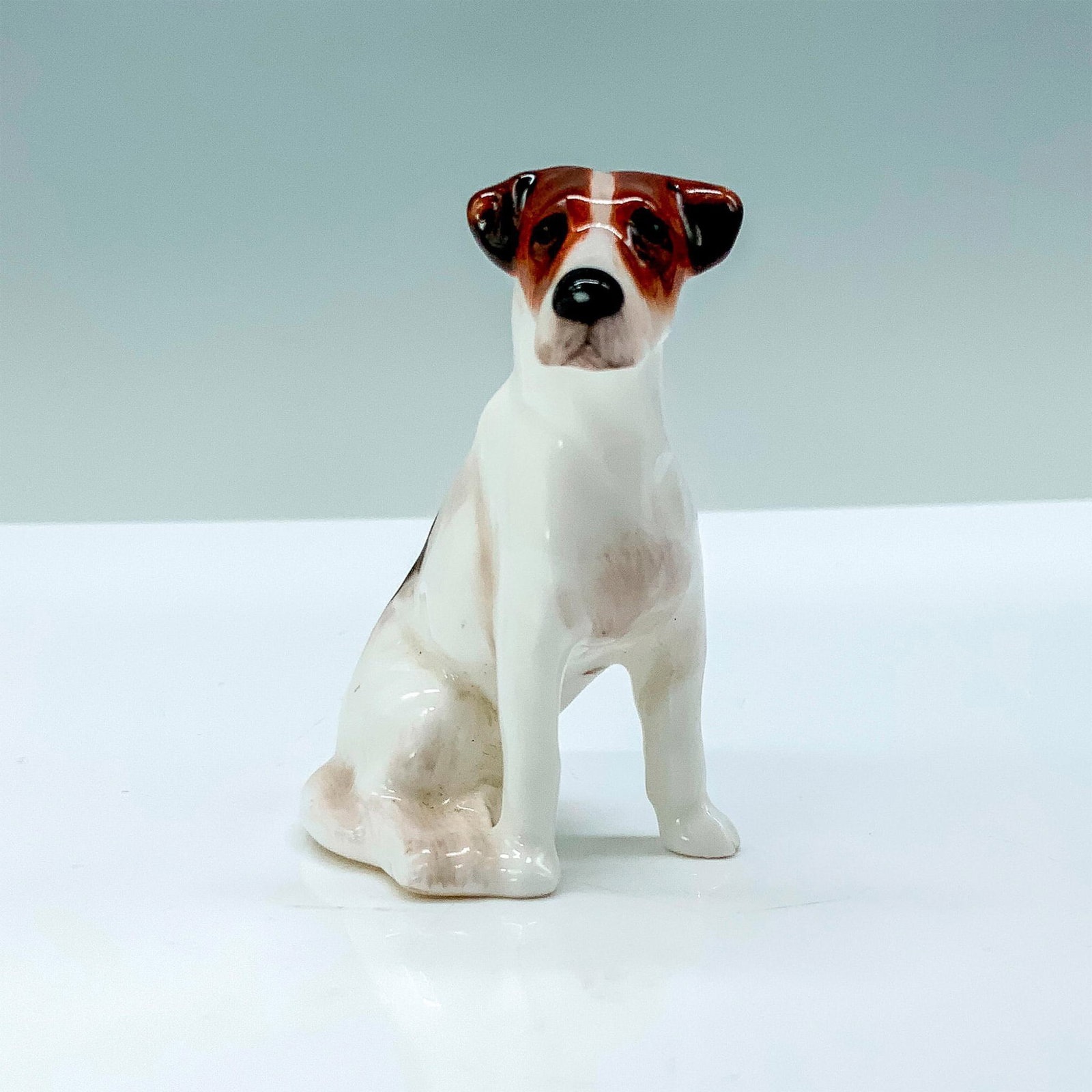 American Foxhound K75 - Royal Doulton Dog Figure: A porcelain American Foxhound that has white, brown, and black fur sitting on its hind legs. Royal Doulton backstamp. Issued: 1931-1977 Dimensions: 1.5"L x 1.25"W x 2.5"H Manufacturer: Royal Doulton C