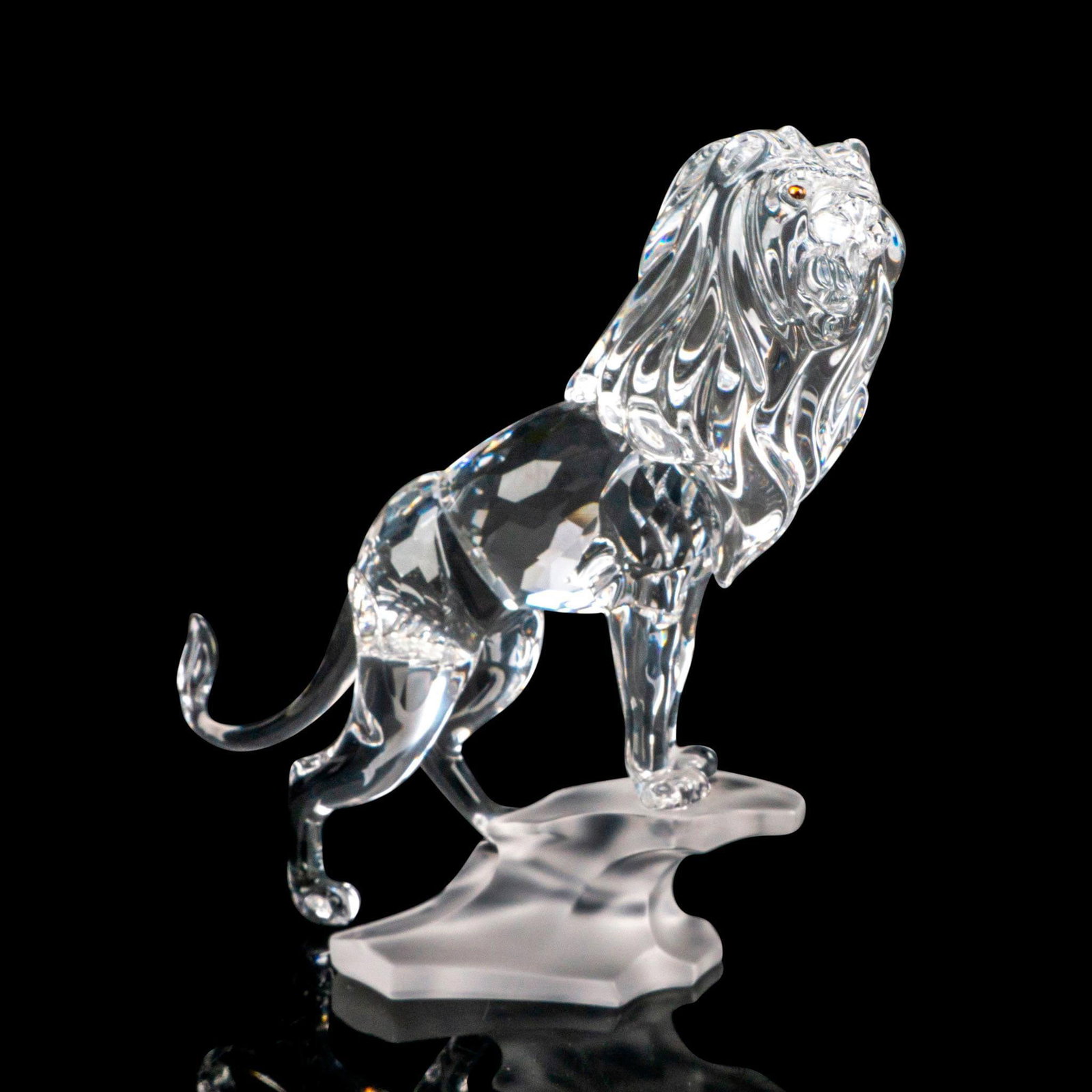 Swarovski Crystal Figurine, Lion: Part of the Rare Encounter collection. Depicting a clear crystal lion with amber crystal eyes, standing on a frosted rocky base. Swarovski marking. This item has its original box: 7.5"L x 6"W x 8"H. A
