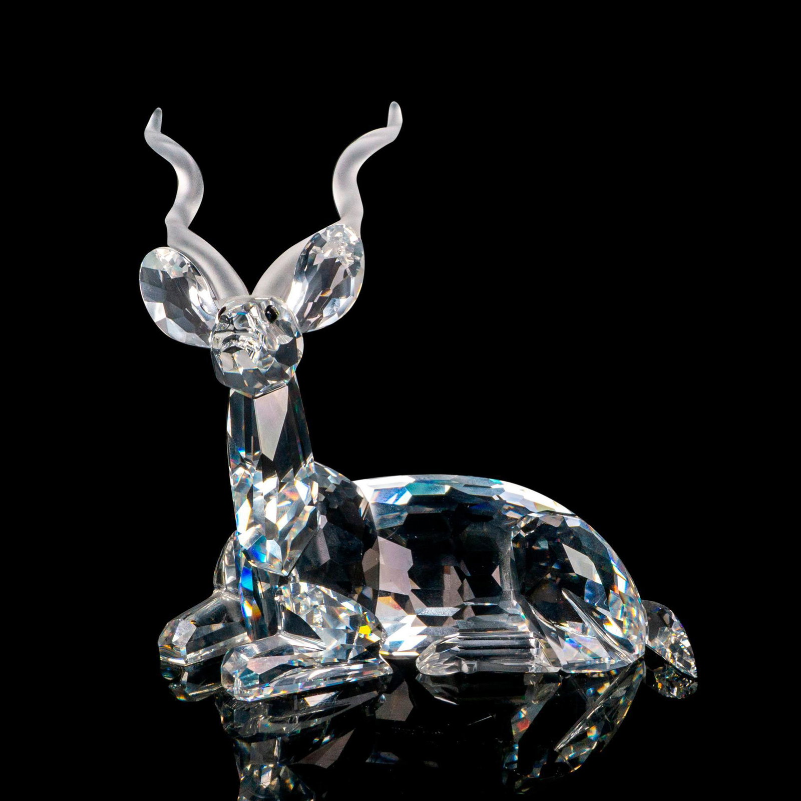 Swarovski Crystal Society Figurine, The Kudu: Part of the Inspiration Africa collection, depicts a clear crystal figure of an antelope resting with frosted horns. Swarovski markings. This item has its original box: 7.5"L x 7.5"W x 6.5"H. Dimensio