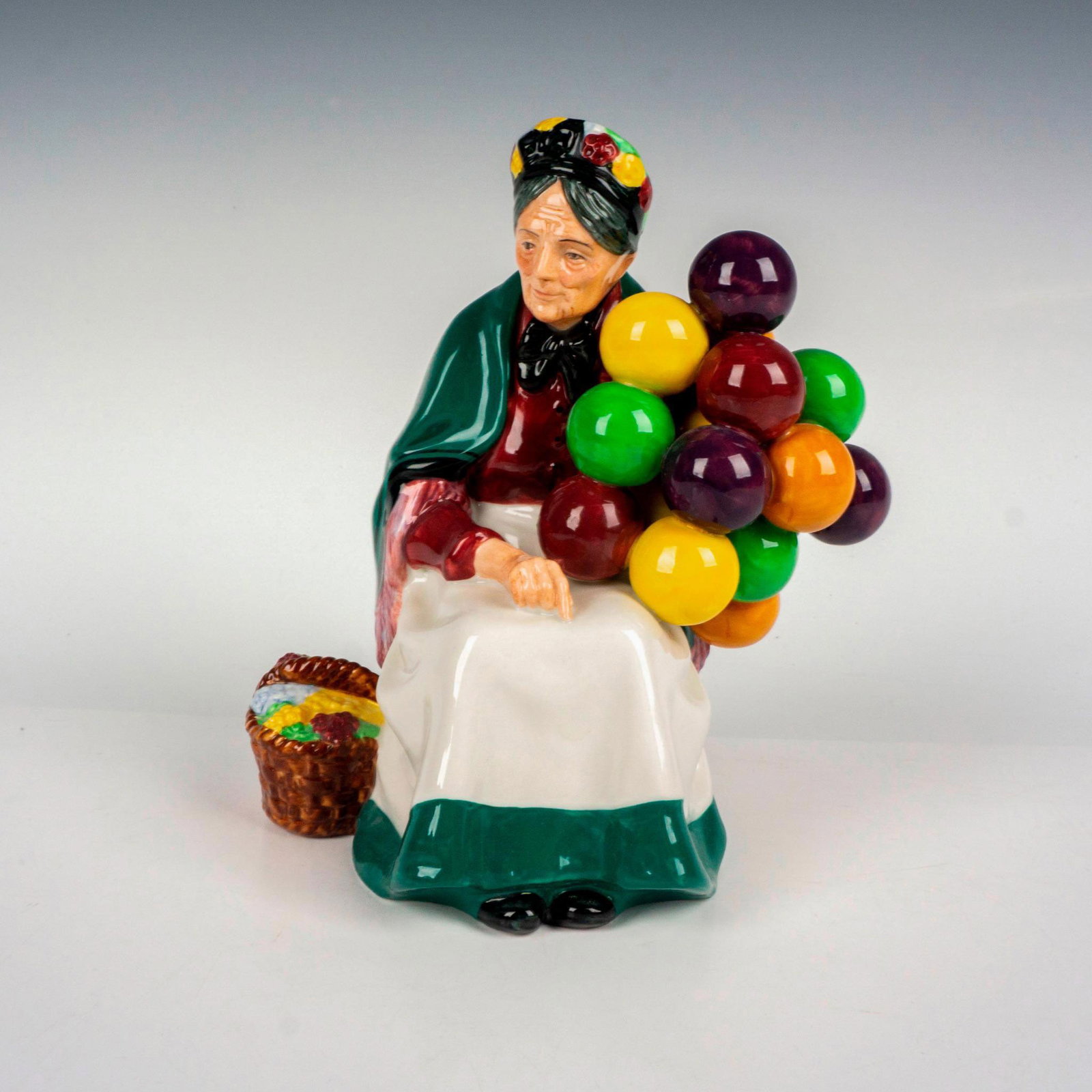 Old Balloon Seller - HN1315 - Royal Doulton Figurine: Part of the Street Vendor collection. Older lady sits holding colorful balloons, basket at her side. Royal Doulton backstamp. Artist: Leslie Harradine Issued: 1929 - 1998 Dimensions: 7.5"H Manufacture