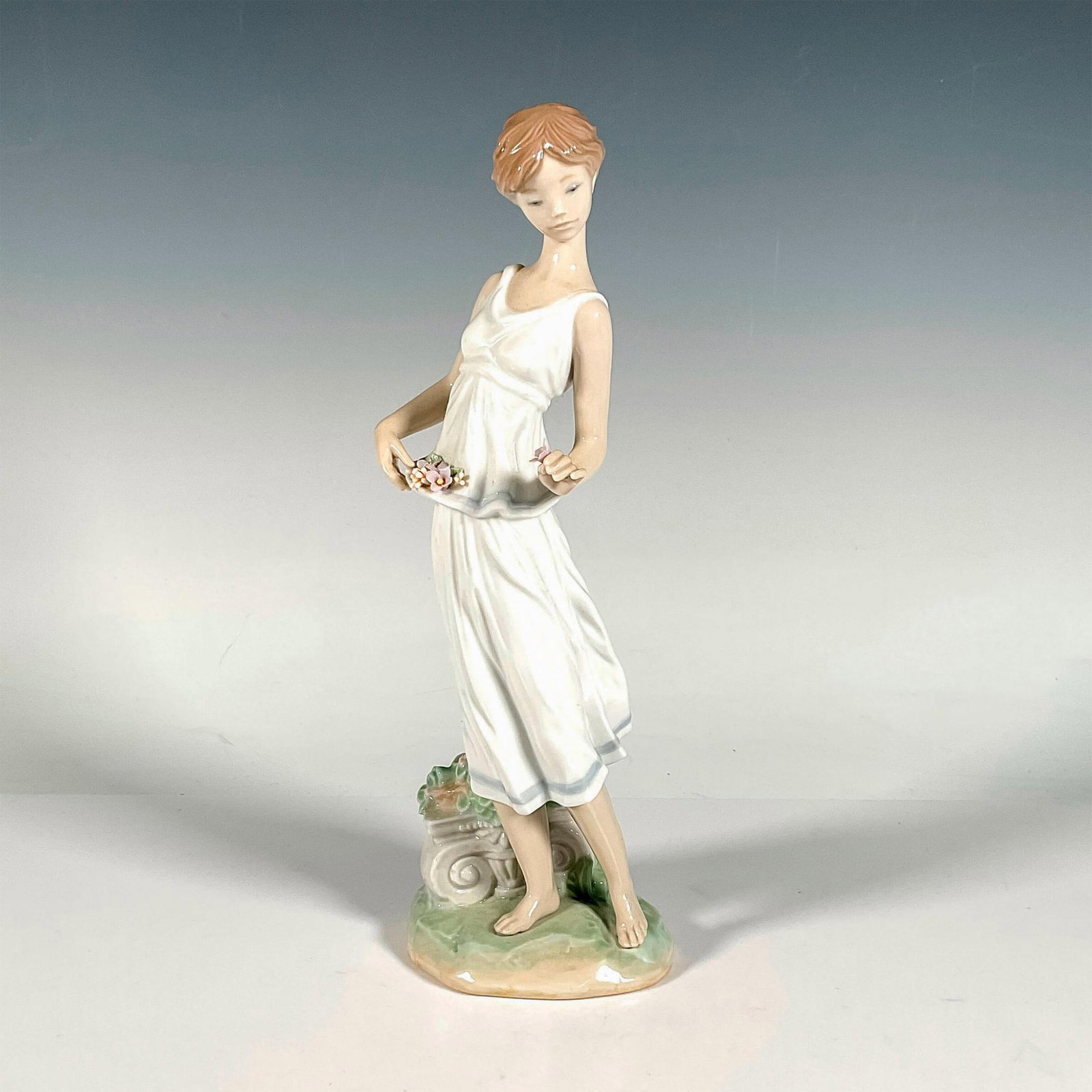 Flowers For A Goddess 1007709 - Lladro Porcelain Figurine: Glossy finish; Lladro backstamp. Includes original box. Box measures: 13.5"L x 7"W x 7.25"H. Artist: Virginia Gonzalez Issued: 2006 - 2007 Dimensions: 10.75"H x 3.25"W Manufacturer: Lladro Country of