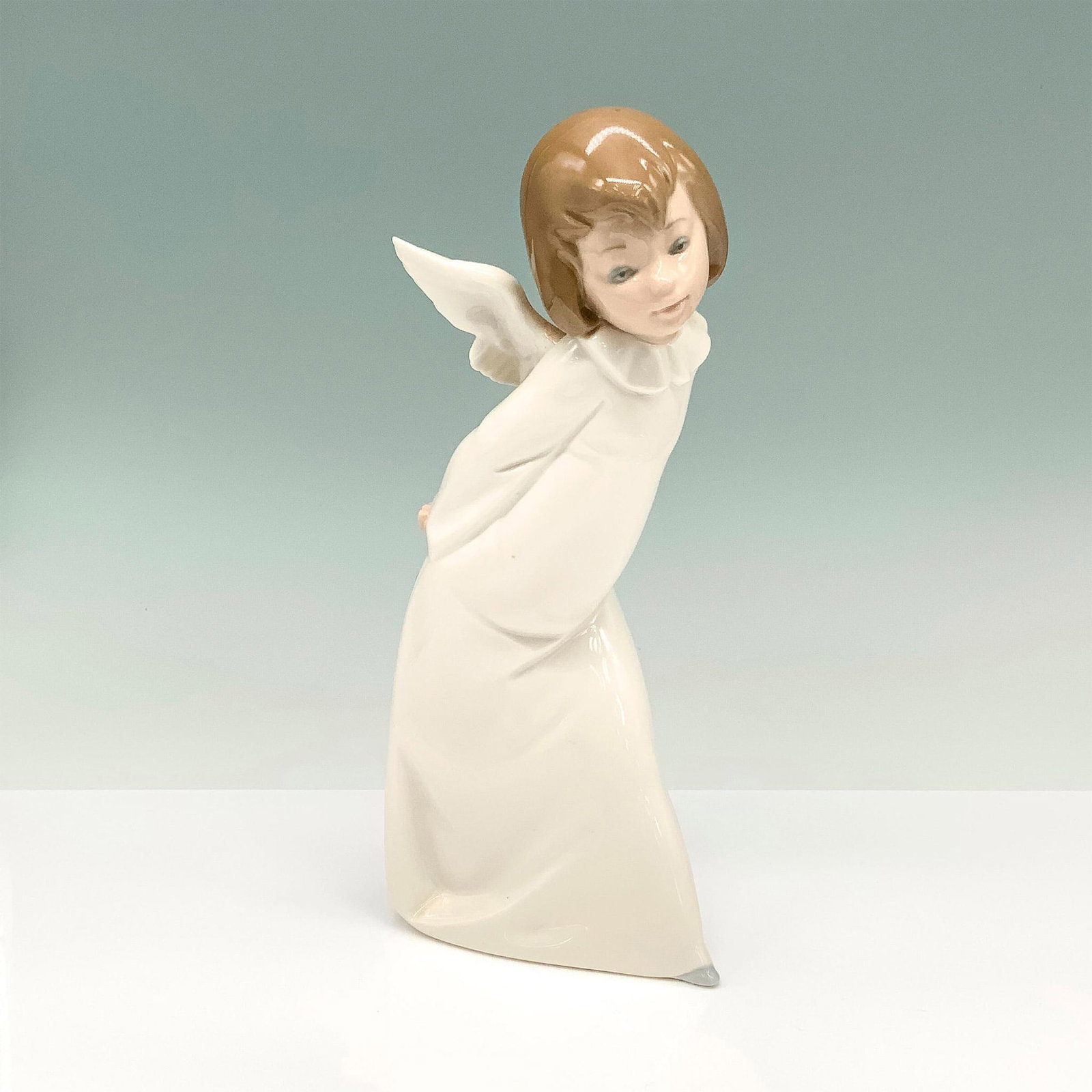 Curious Angel 1004960 - Lladro Porcelain Figurine: Angel Farolero with glossy finish and Lladro backstamp. This angel with small wings on her back and a full-length white dress is bent over to look at something. Artist: Salvador Debon Issued: 1977 Dim