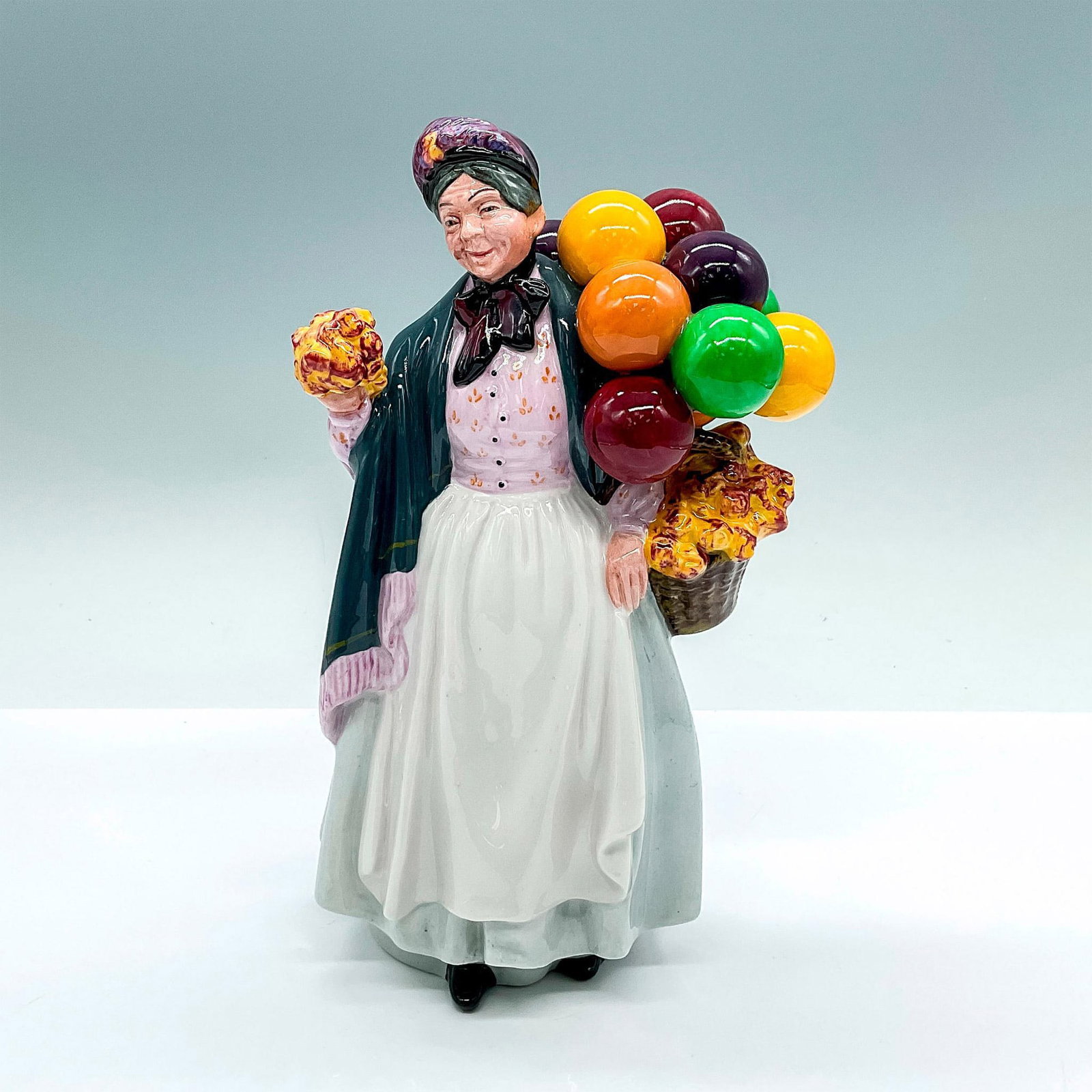 Biddy Penny Farthing - HN1843 - Royal Doulton Figurine: Hand decorated figure of a woman in a gray shawl holding balloons and flowers. Royal Doulton backstamp. Artist: Leslie Harradine Dimensions: 5.5"L x 4"W x 8.5"H Manufacturer: Royal Doulton Country of 