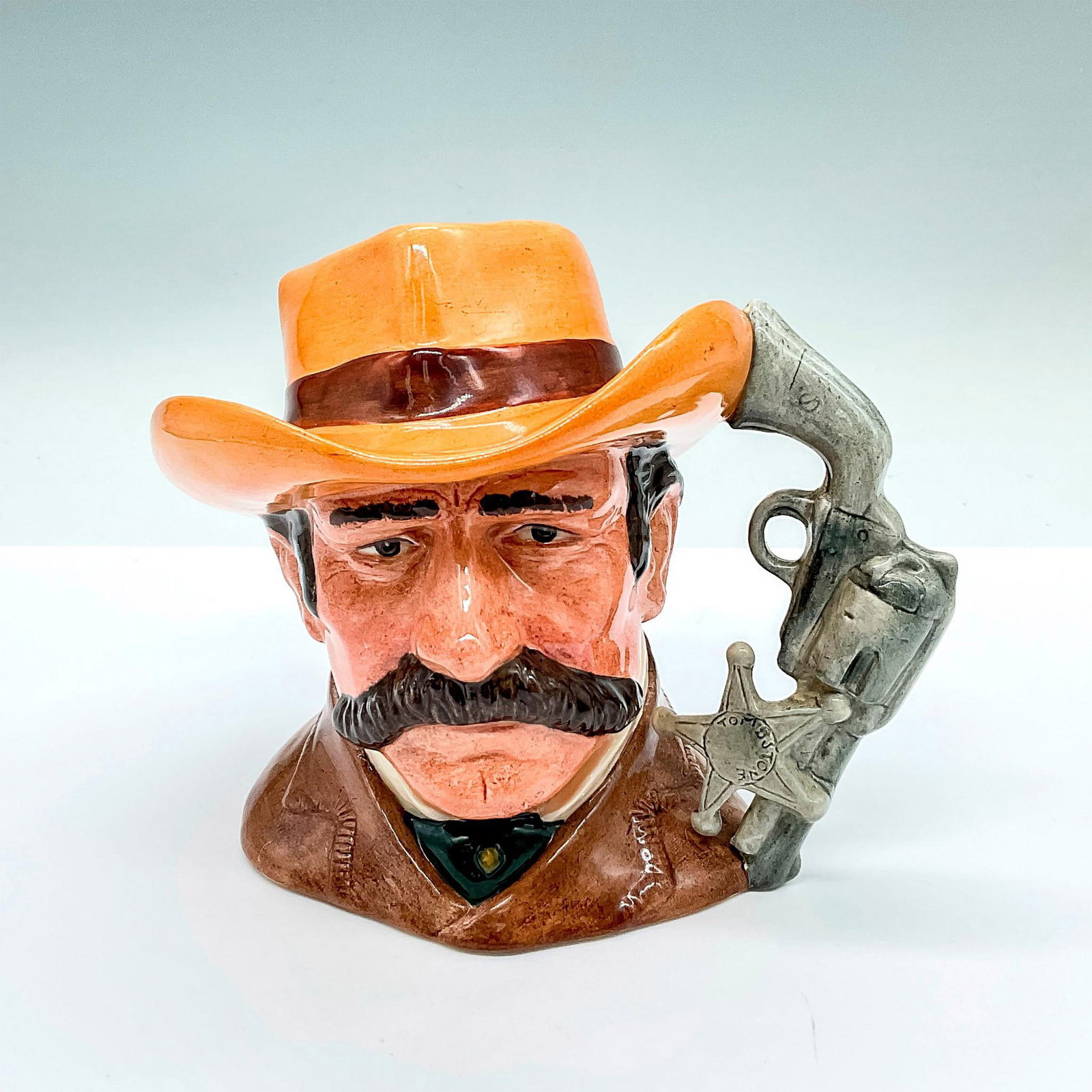 Wyatt Earp D6711 - Royal Doulton Odd Character Jug: Part of the Wild West Collection; brown coat, light brown hat with a brown band. Gun and sheriff's badge handle. Royal Doulton backstamp. Artist: Stanley James Taylor Issued: c. 1985-1989 Dimensions: 