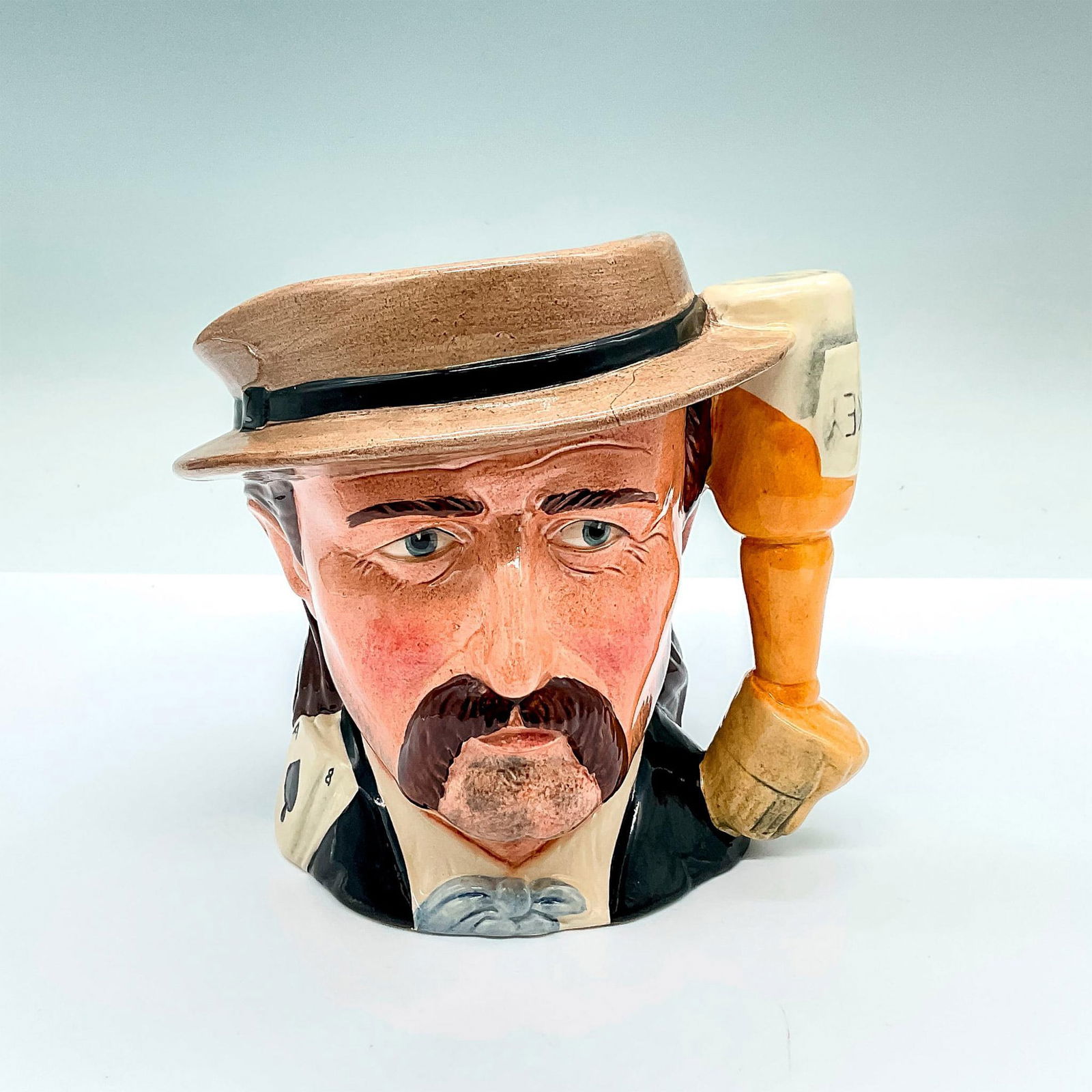 Wild Bill Hickock D6736 - Royal Doulton Odd Character Jug: Part of the Wild West Collection; brown hat, blue tie, and black jacket; upturned whiskey bottle into a glass handle. Royal Doulton backstamp. Artist: Michael Abberley Issued: c. 1985-1989 Dimensions: