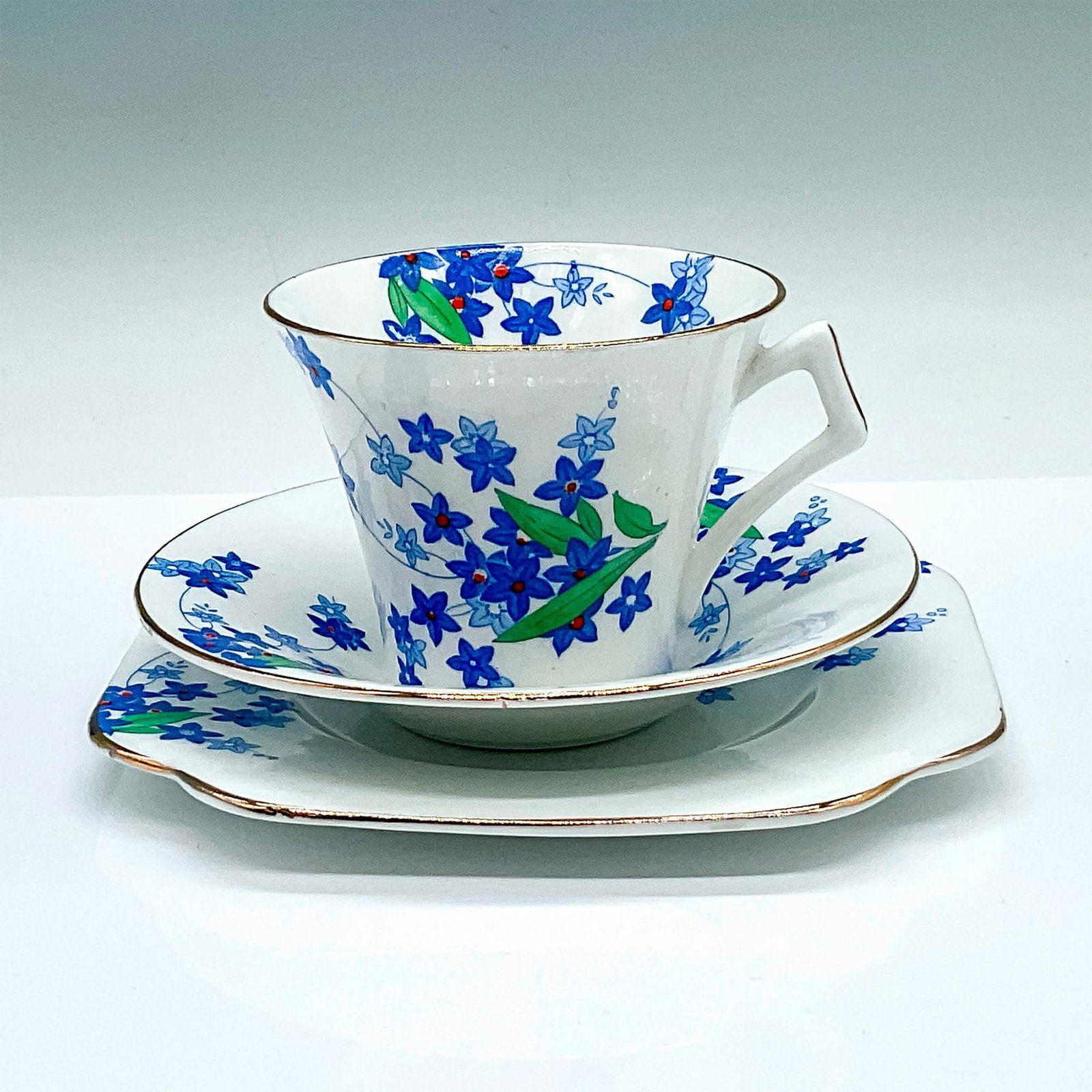 Colclough Bone China Blue Floral Tea Trio No. 4117: White cup, saucer, and dessert plate. Decorated with blue star-shaped flowers and gilded trims. Colclough backstamps. Cup: 4"L x 3.25"W x 2.75"H. Saucer: 5.25"W x 1"H. Dessert plate: 6"L x 6"W x 0.5"H