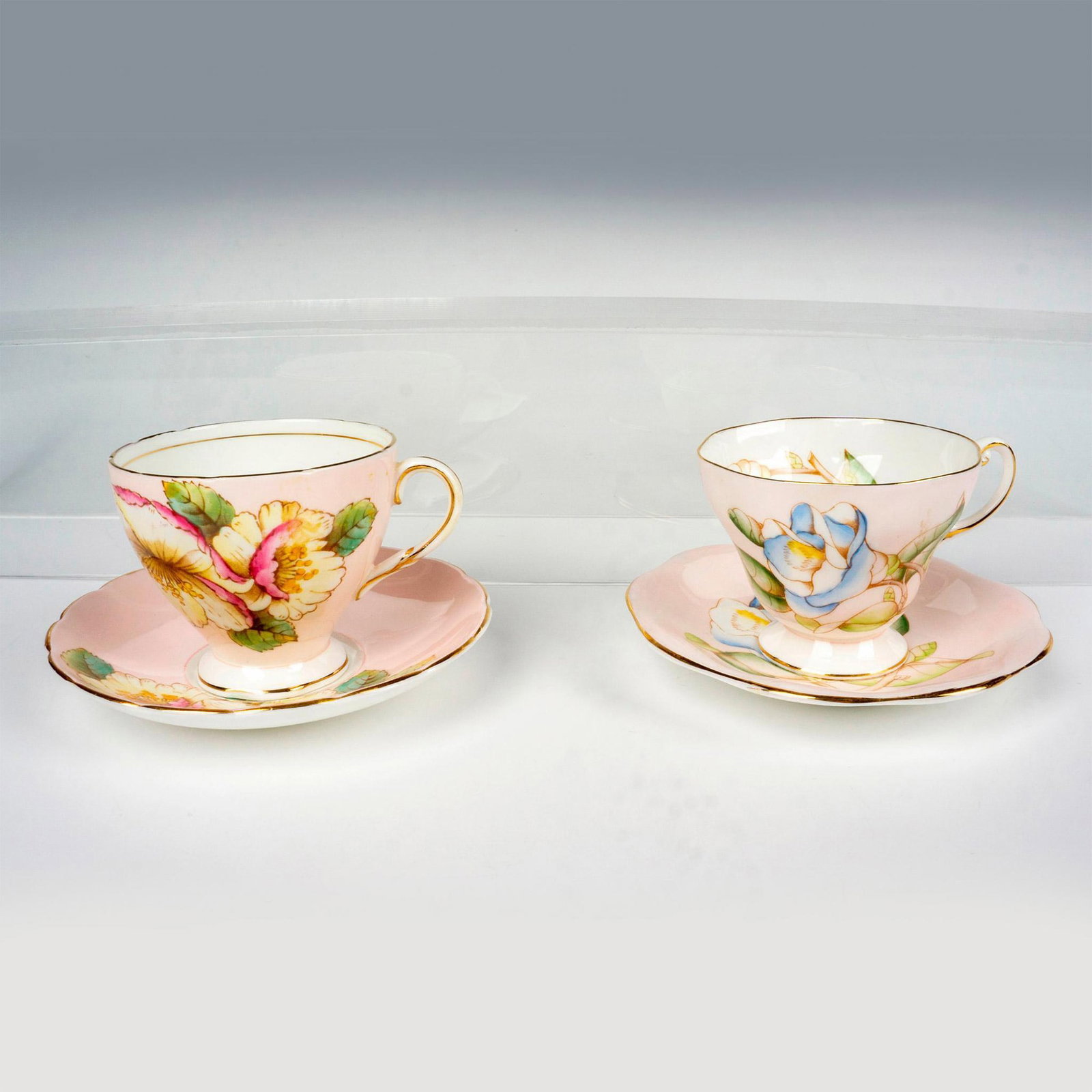 4pc EB Foley Bone China Floral Teacups and Saucers: 2 pink cups and 2 saucers with gilt trims. A set adorned in the Magnolia blue rose pattern, and the other set in a Cherry Blossom pattern. EB Foley Bone China backstamp. Magnolia: (cup) 4.5"L x 3.5"W 