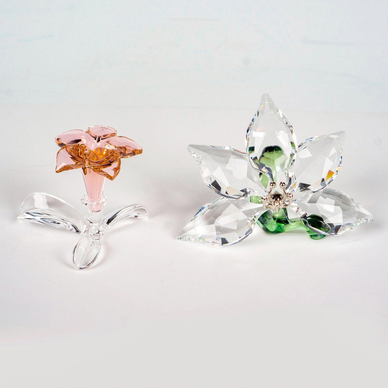 2pc Swarovski Crystal Figurines, Desert Rose + Orchid Flower: Lead crystal SCS membership renewal gifts. Made from colored crystal and silver- tone accents. Swarovski etched backstamp. Orchid measures: 2.5”W x 1.5”H. Desert Rose measures: 1.25”