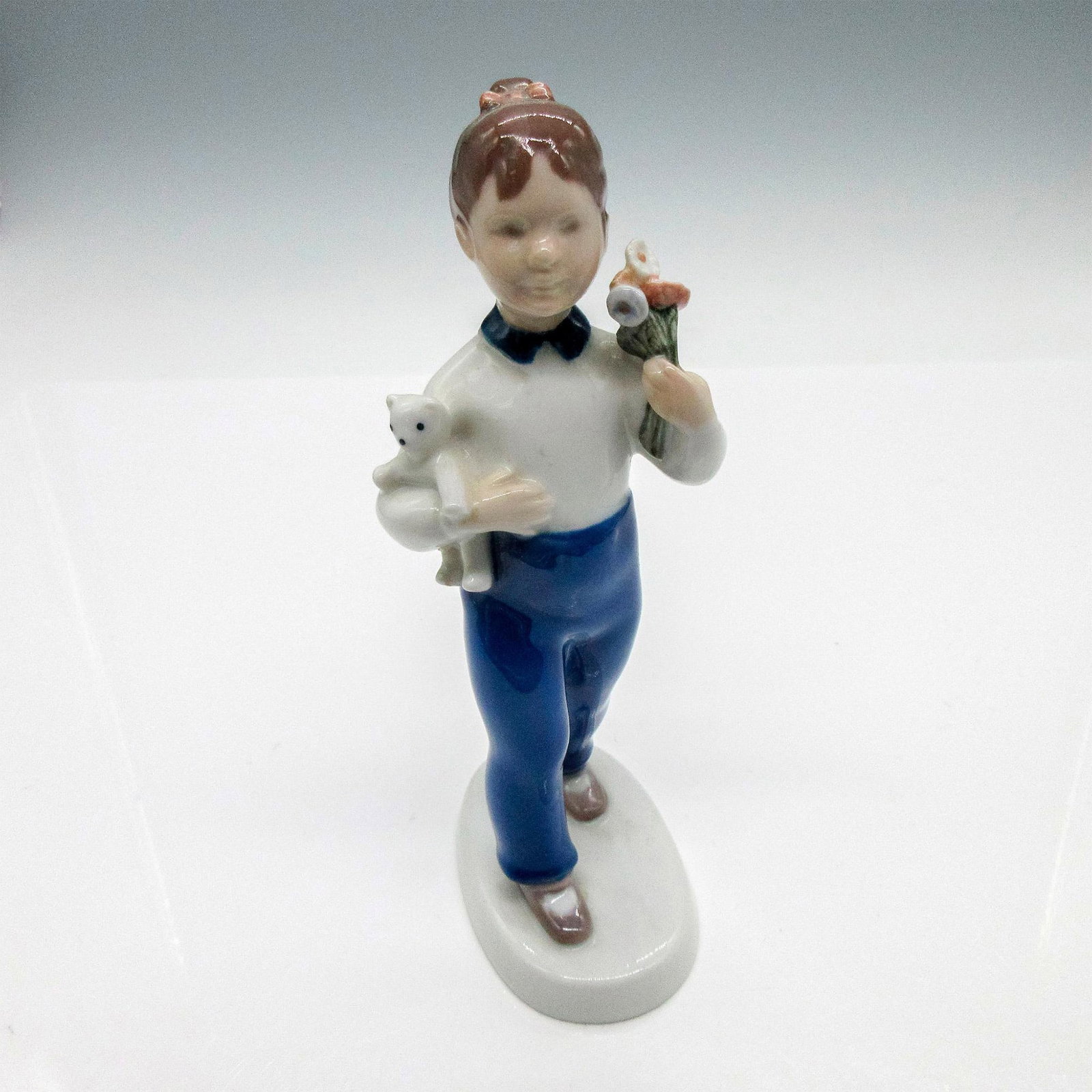 Bing & Grondahl Porcelain Figurine, Girl with Flowers: Glossy figurine depicting a young girl with flowers and a teddy bear in her arms. Copenhagen figurine#2398. Bing & Grondahl backstamp. Issued: 20th century Dimensions: 2.75"L x 3.50"W x 7"H Edition Nu