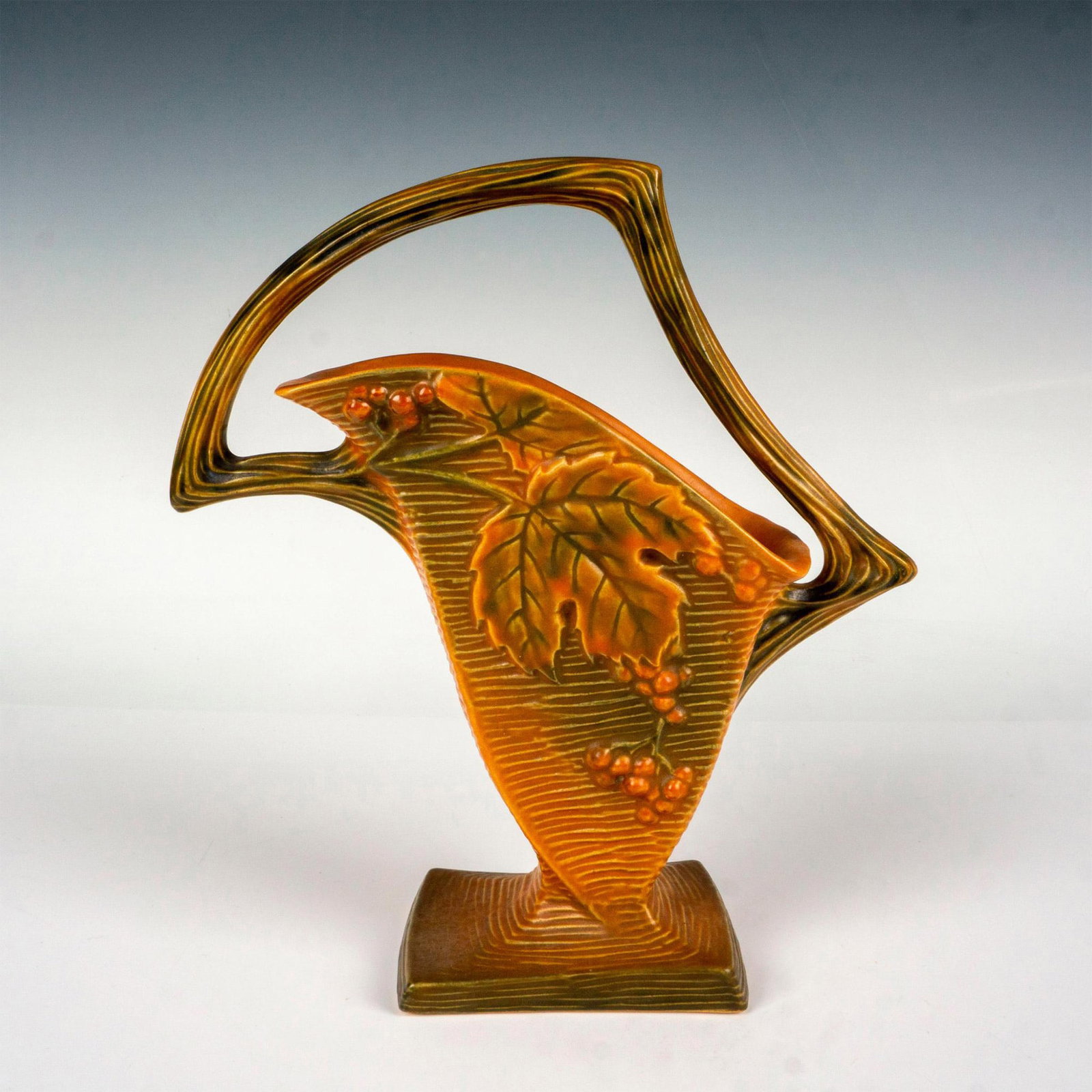 Roseville Pottery Vase, Bushberry: A beautiful decorative vessel decorated with a raised pattern of bush berries and leaves with a vine handle. Roseville backstamp. Dimensions: 9.5"L x 3.75"W x 10.5"H Manufacturer: Roseville Country of