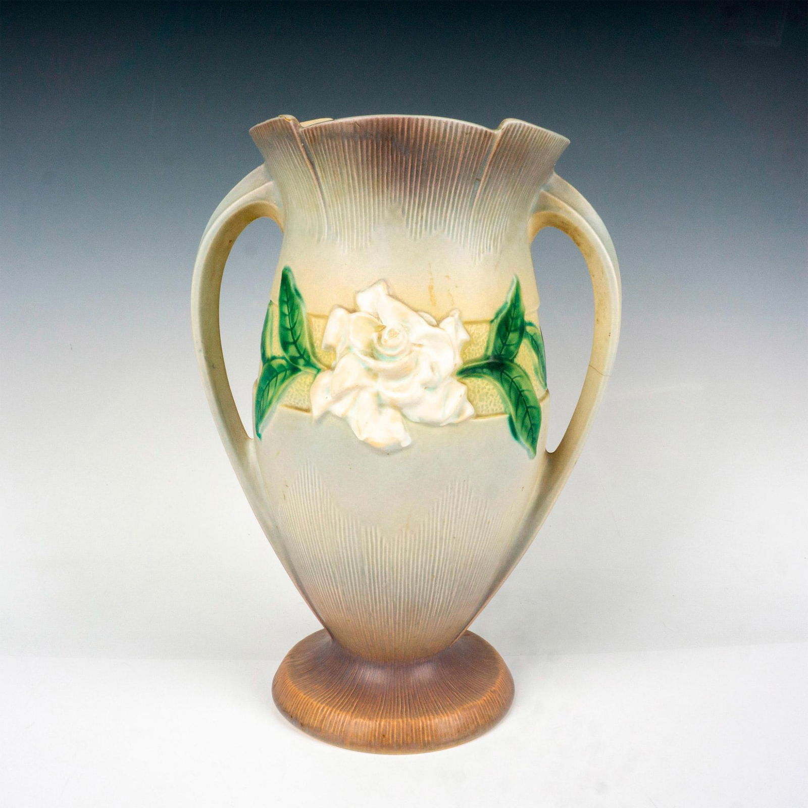 Roseville Pottery Vase, Gardenia Grey: Matte finished, double handled vase colored grey with hints of peach and lavender. Center is accented with raised flower and green leaves. Roseville raised mark. 689-14. Manufacturer: Roseville Countr