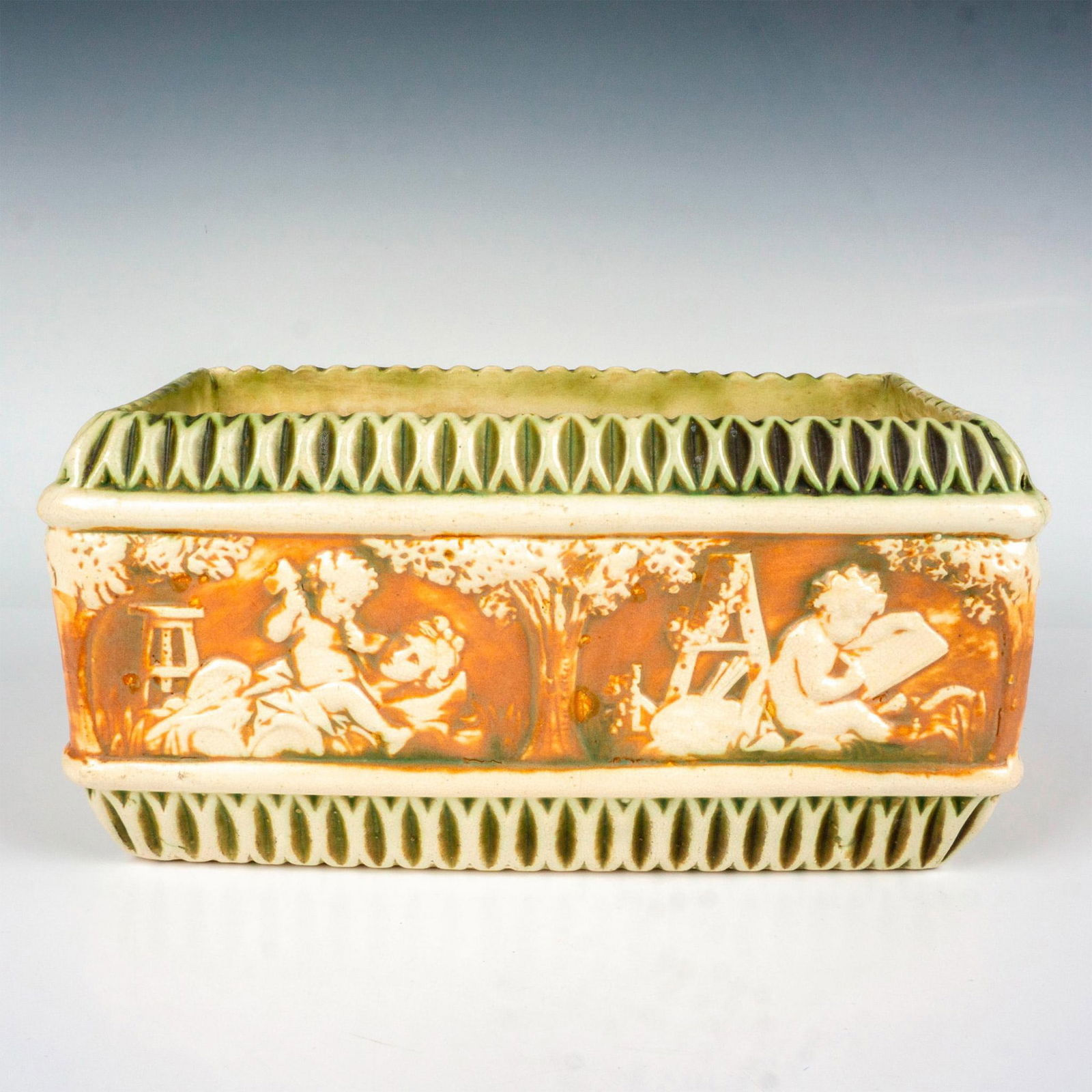 Roseville Pottery Planters, Donatello: A rectangular planter with creamed colored Corinthians and cherubs set against brown ground. Artist: Frederick Rhead Issued: c. 1915 Dimensions: 11.75"L x 6.25"W x 5.75"H Manufacturer: Roseville Coun