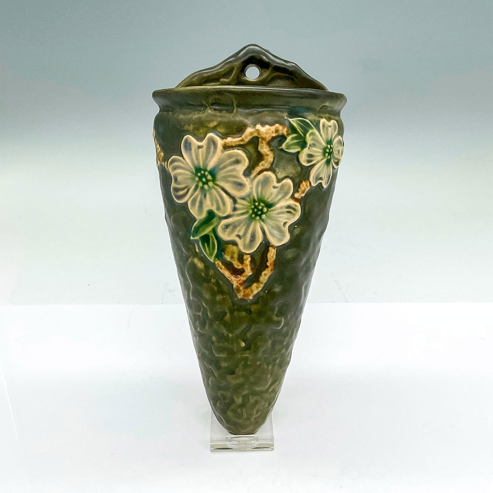 Roseville Pottery Wall Pocket, Dogwood, Textured: Earthenware wall vase in a pattern that features flowering dogwood branches of white flowers on a textured sage green background. Roseville R stamp on back. Issued: circa 1926 Dimensions: 9.25"H x 4.5