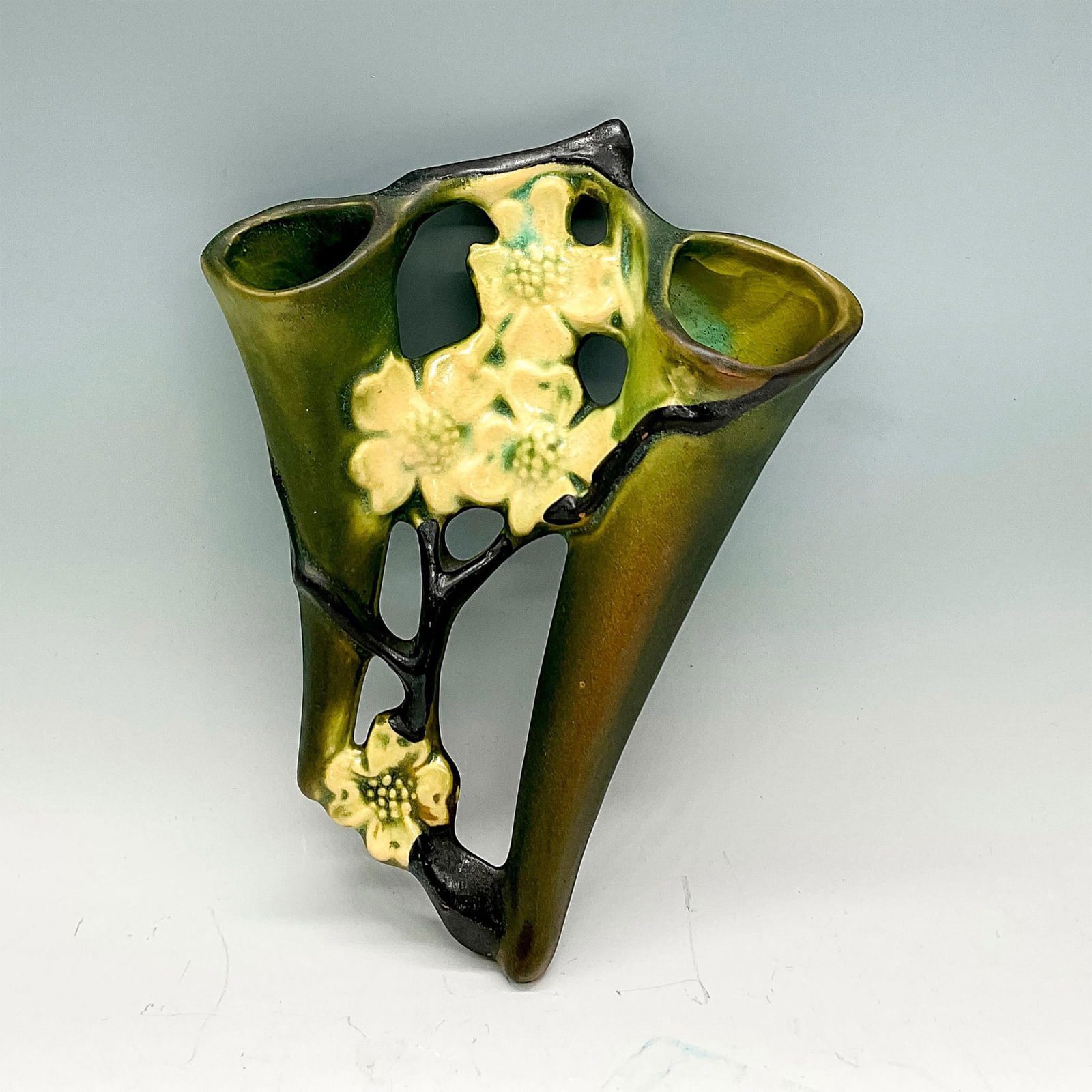 Roseville Pottery Wall Pocket, Dogwood: Earthenware wall vase in a pattern that features flowering dogwood branches of white flowers on an olive green background. Issued: circa 1920 Dimensions: 9"H x 6.5"W x 2"D Manufacturer: Roseville Coun