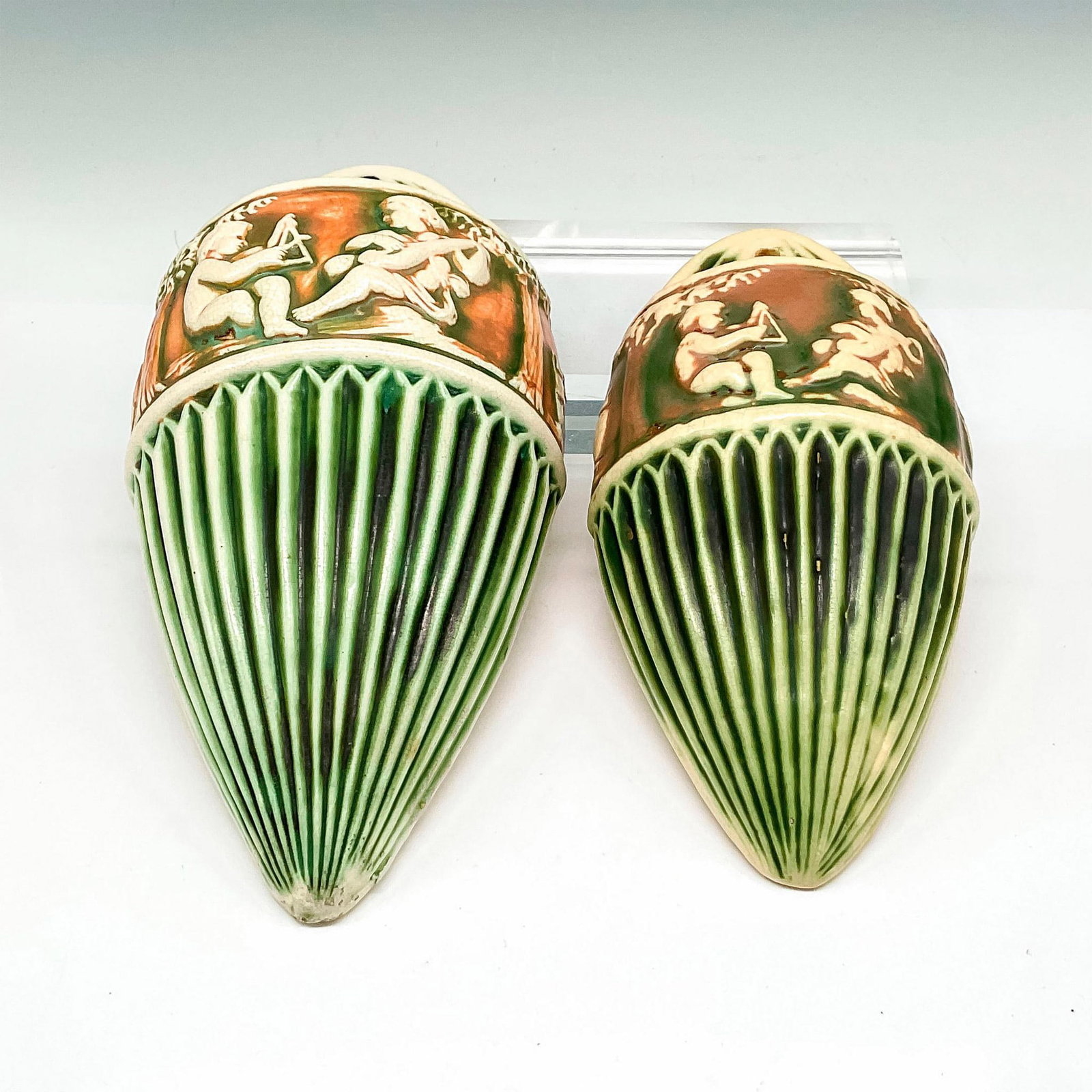2pc Roseville Pottery Wall Pockets, Donatello Green: Conical, ribbed pottery finished with light glaze over green and rust coloration. Banded design of seated cherubs playing instruments. Donatello RP impressed mark. Largest piece: 5.25"L x 3"W x 11.5"H