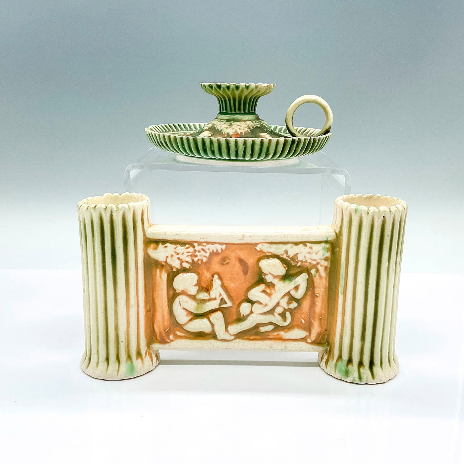 2pc Roseville Pottery Candle Holder and Vase, Donatello: A candlestick holder, and a double vase with green and creamed colored Corinthians and cherubs set against brown ground. Candle holder: 5.5"W x 2"H. Vase: 8"L x 2"W x 4.25"H. Issued: c. 1915 Manufactu