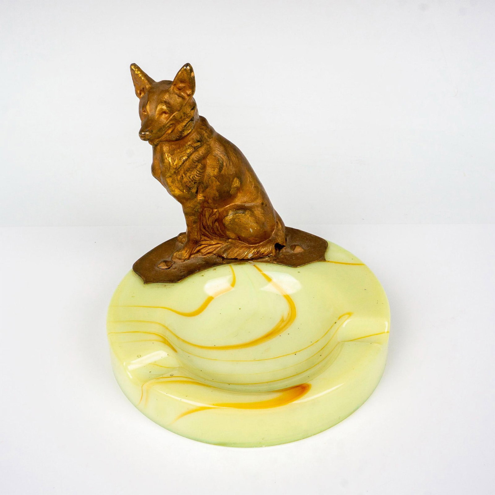 Antique Akro Agate Metal Figural Ashtray, Alsatian: Yellow agate glass tray with a golden brown swirl pattern. It has a gold-tone metal figure of a sitting dog; mounted and screwed. Issued: c. 1930 Dimensions: 5.5"W x 5.5"H Manufacturer: Akro Agate Gla