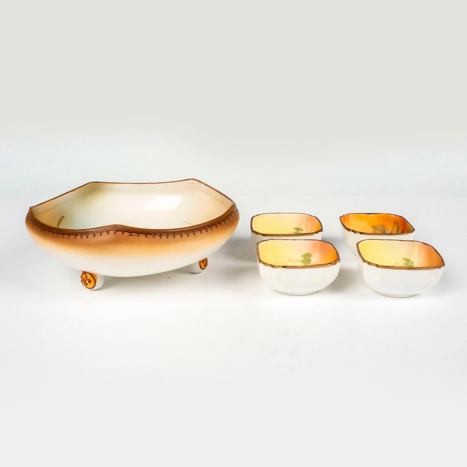 5pc Nippon Porcelain Bowl and Salt Cellars: A set of 4 small square salt cellars, and 1 nut bowl. Featuring naturalistic painting of a peanut. Nippon backstamps. Salt cellar: 2.25"L x 2.25"W x 1"H. Nut bowl: 6.5"L x 6.5"W x 2.5"H. Issued: c. 19