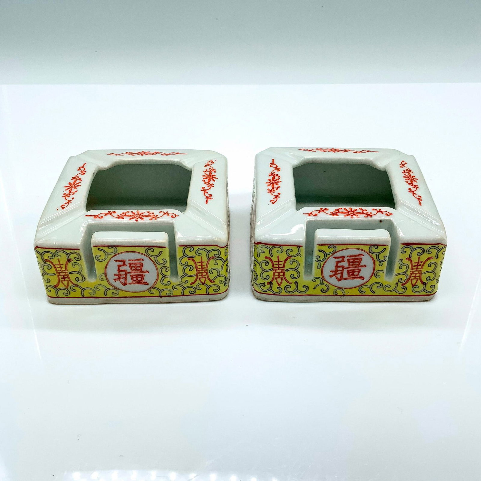 Pair of Vintage Chinese Match Holder Ashtrays: Two ceramic ashtrays with a slot for matches. They are decorated with a red and yellow floral motif and Chinese writing. Dimensions: 3.25"L x 3.5"W x 1.5"H